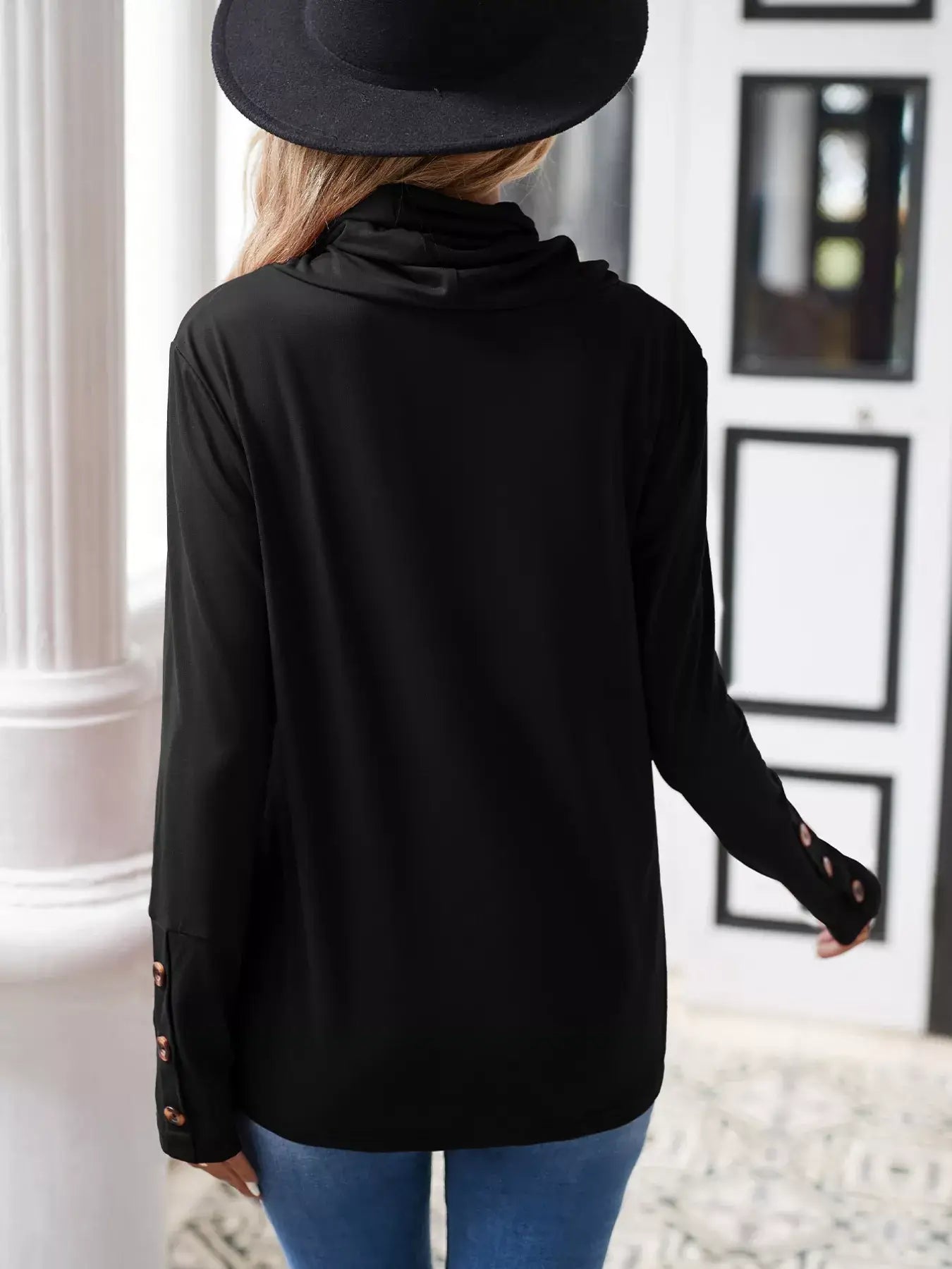 Back view of a woman wearing a cowl neck long sleeve blouse in black, showcasing its elegant design and button details.