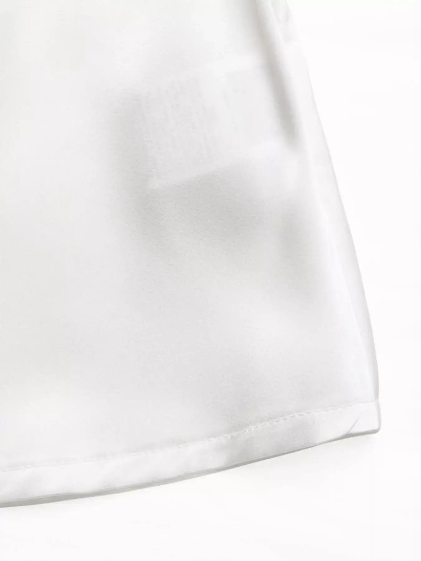 Close-up of the fabric hem of the Ruffled Cold Shoulder Flounce Sleeve Blouse in white.
