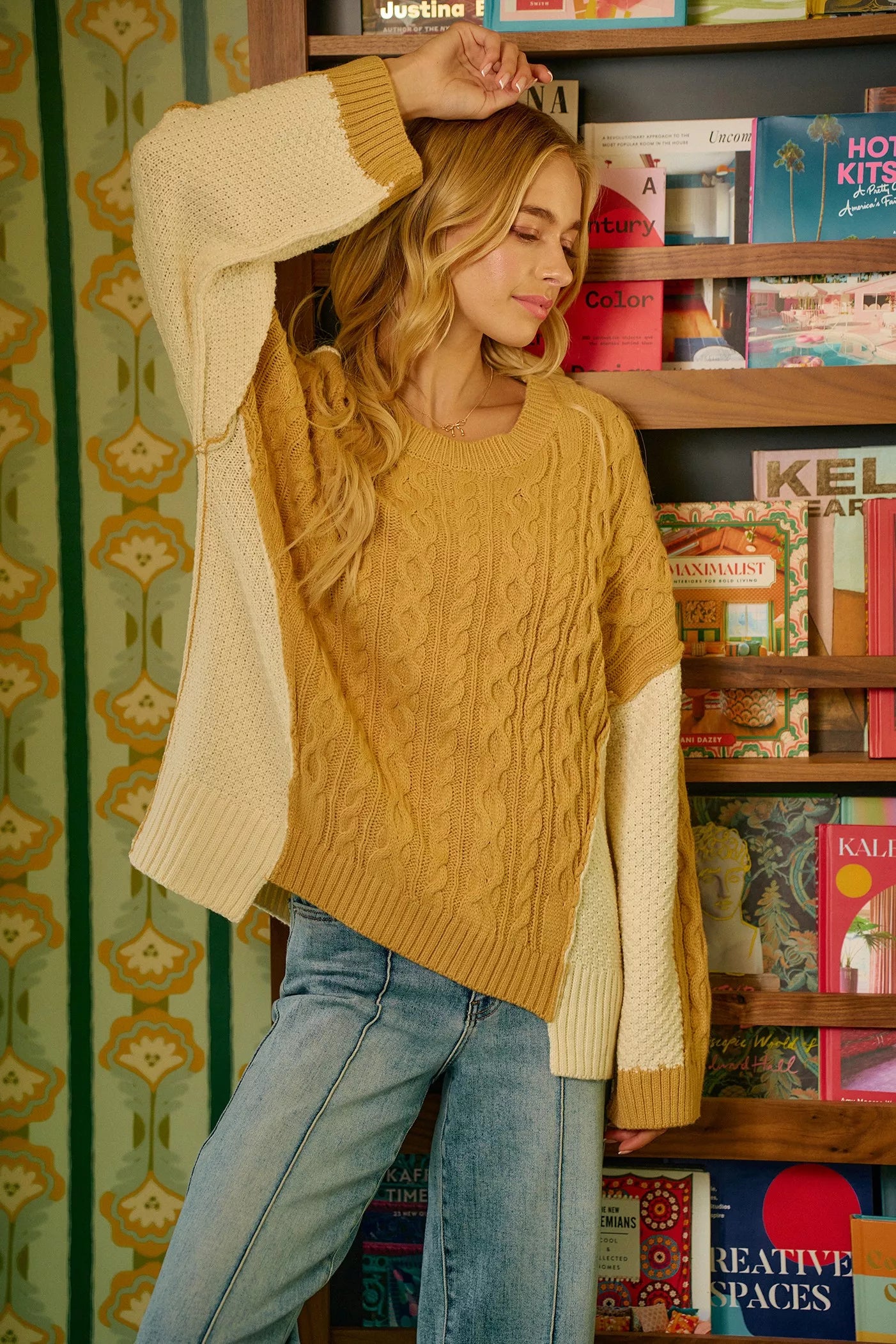 Model wearing BiBi Cable Knit Hacci Combo Sweater with uneven hem and two-tone colors, styled in a cozy interior.