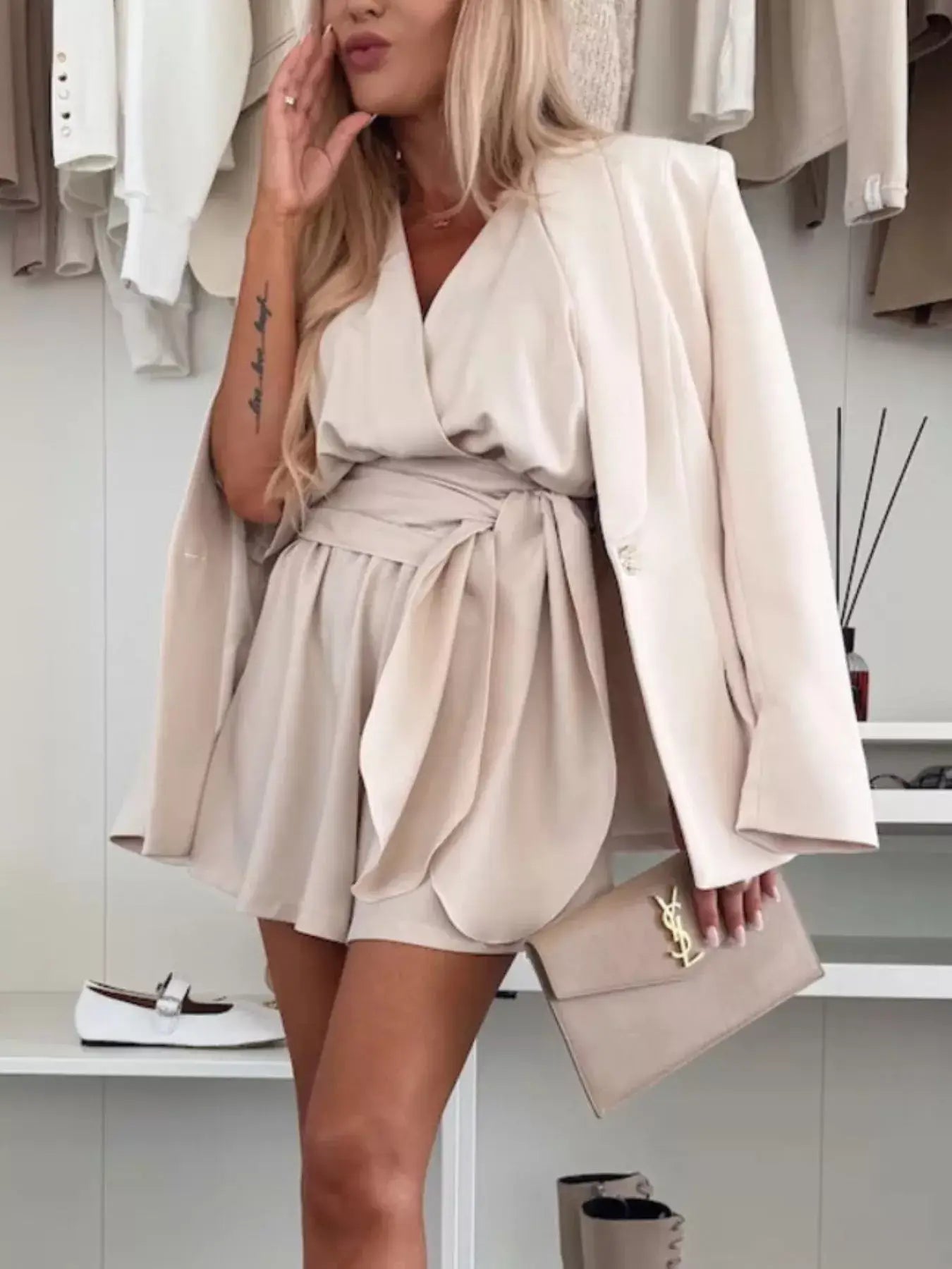 Model wearing a Full Size Surplice Tie Waist Romper with a blazer and clutch bag.