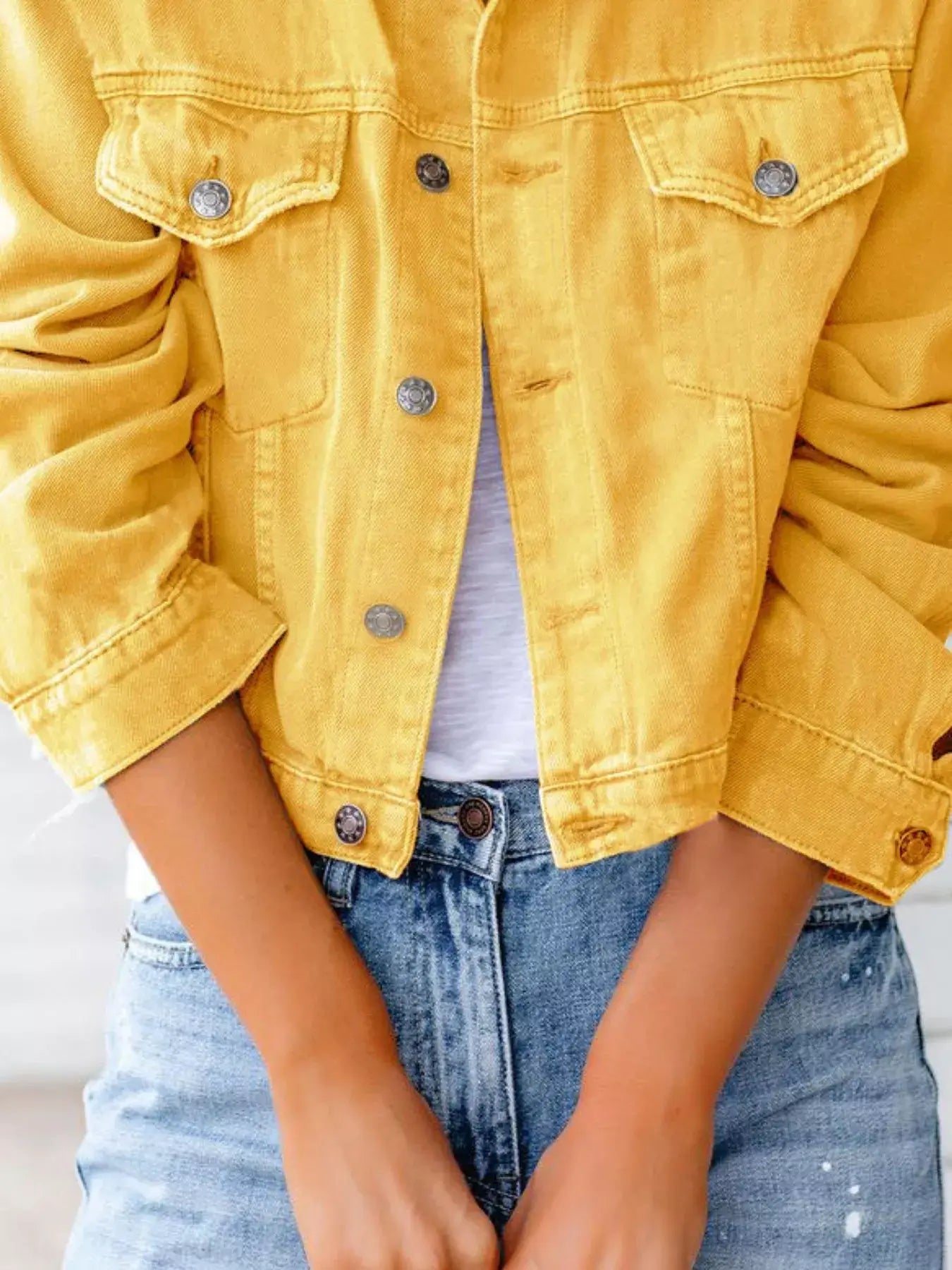 Woman wearing a yellow button-up denim jacket, styled with a white top and blue jeans.