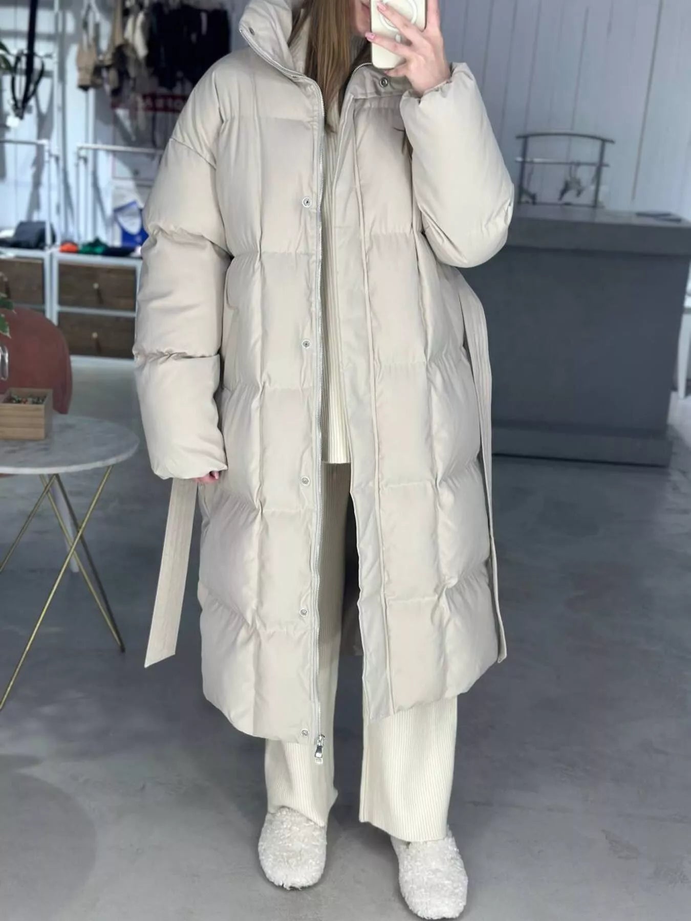 Woman wearing a Longline Padded Winter Coat Belted in beige, featuring pockets, zipper, and a warm-lined design.