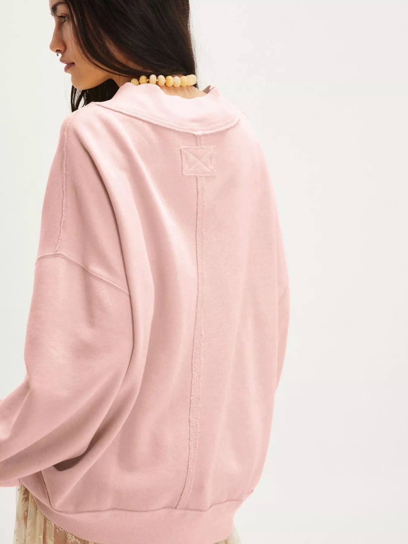 Back view of a woman wearing an Exposed Seam Dropped Shoulder Sweatshirt in pink, showcasing its relaxed fit and dropped shoulders.