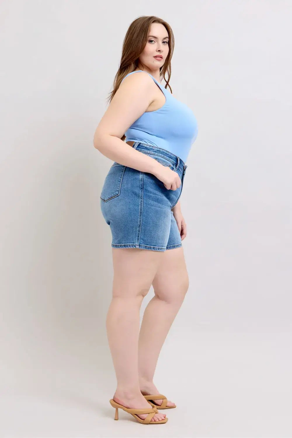Plus size model showcasing Judy Blue denim shorts with pockets, featuring a 2-button design in a casual setting.