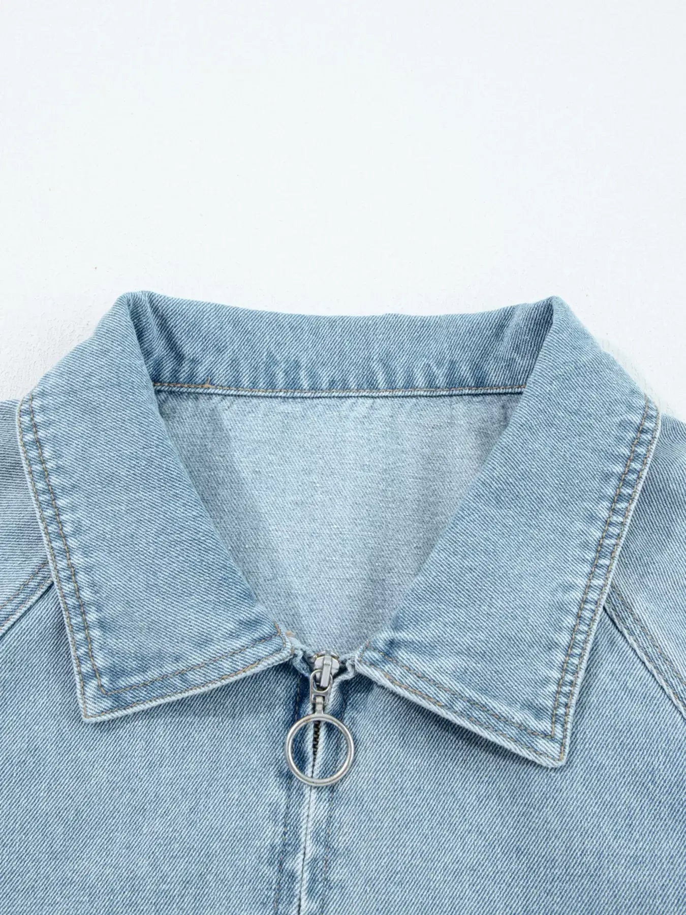 Close-up of the collar and zip of a light blue denim jacket with an elastic edge design.