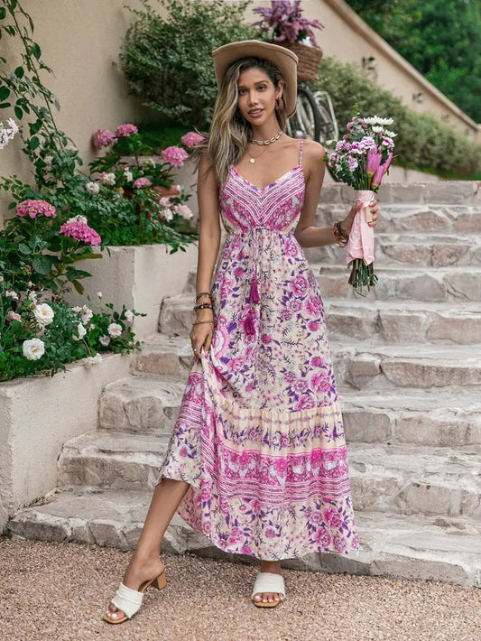 Model wearing a Tassel Printed V-Neck Maxi Dress, holding flowers and standing on steps surrounded by flowers.