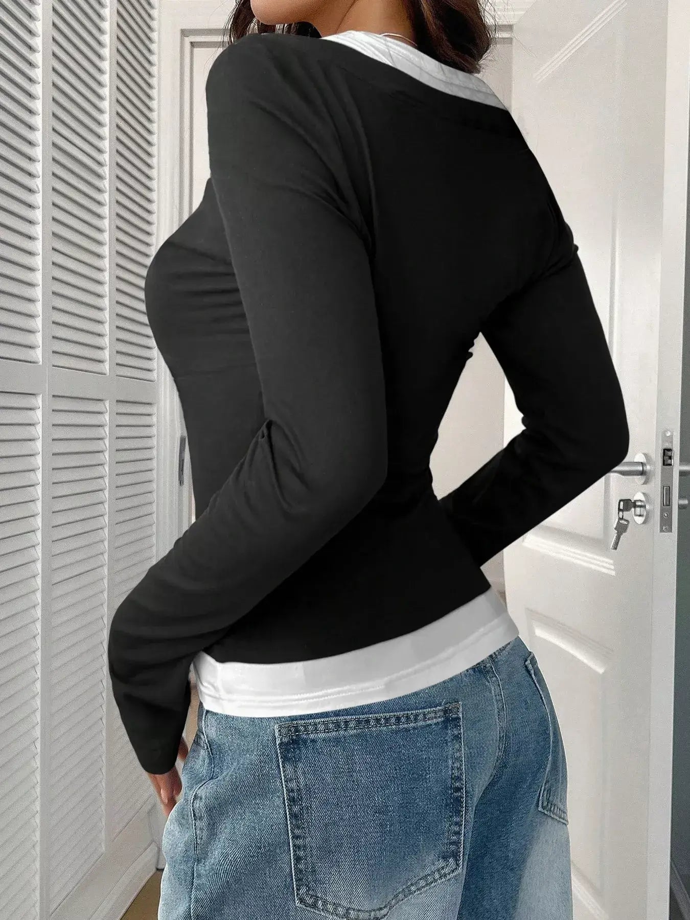 Model wearing a black scoop neck long sleeve t-shirt with a white top underneath, paired with denim jeans.