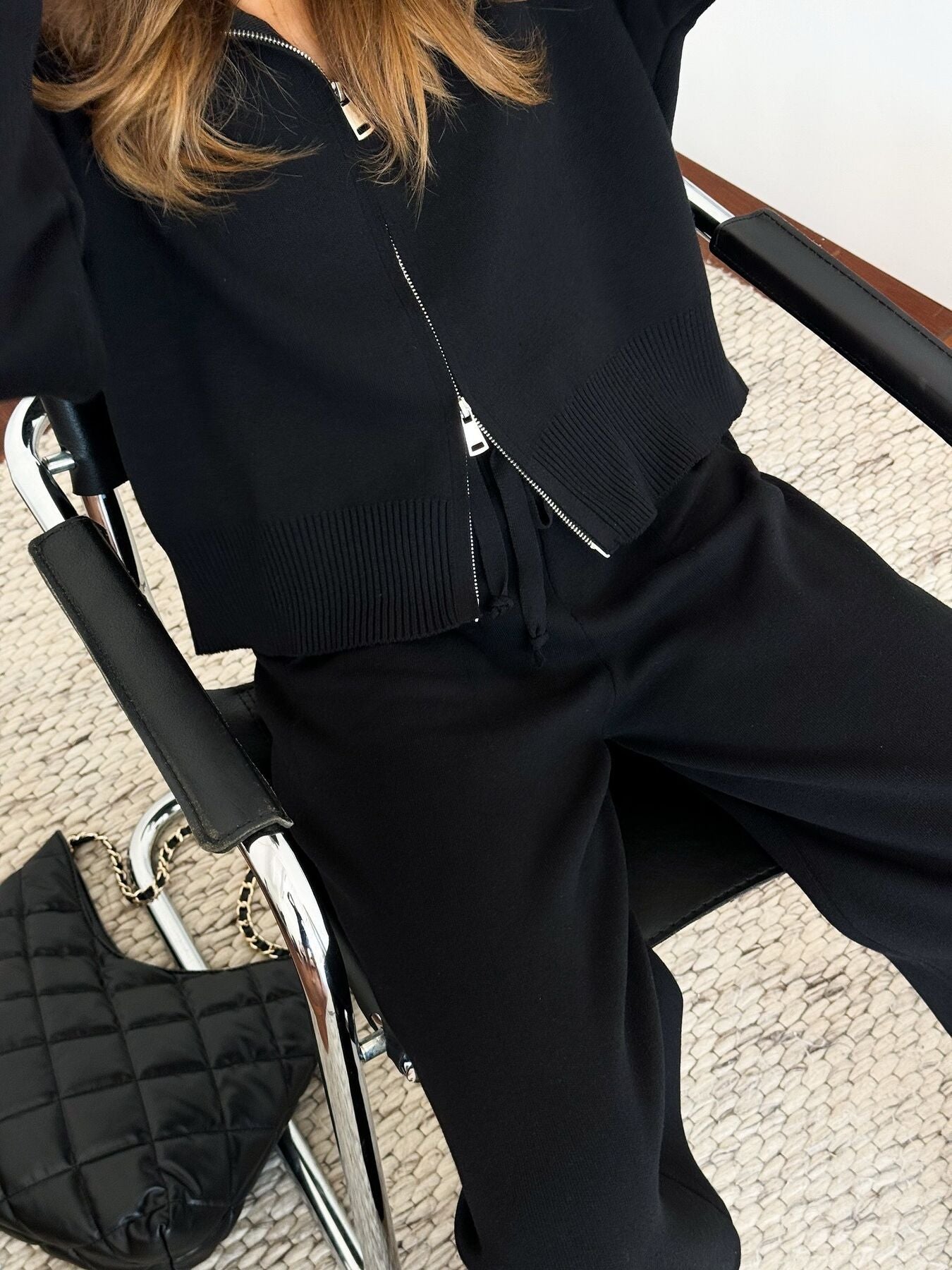 Women wearing Zip Up Cardigan and Wide Leg Pants Knit Set, sitting in a stylish chair with a black handbag.