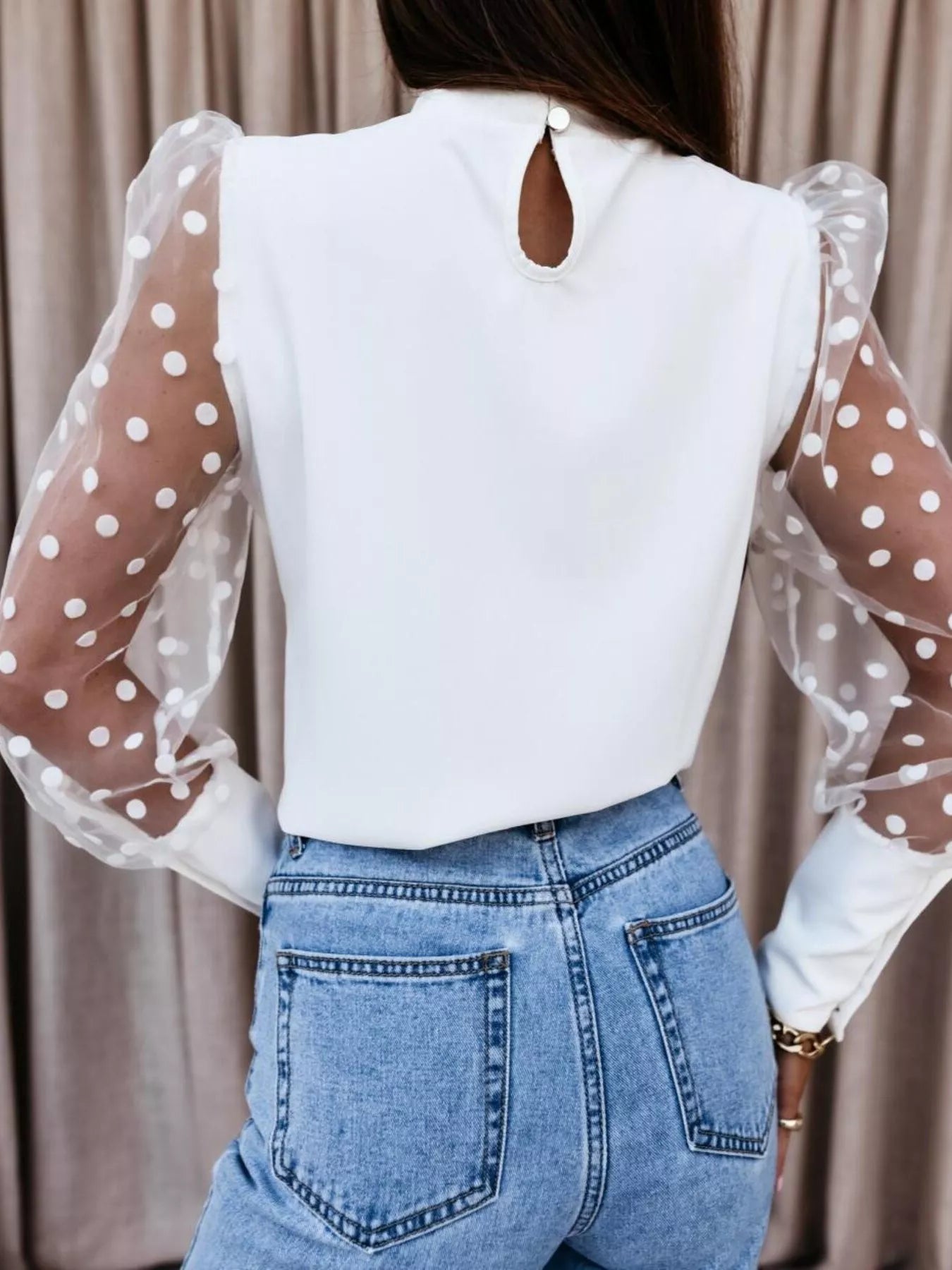 Back view of a woman wearing a Polka Dot Mesh Sleeve Blouse with sheer sleeves and a keyhole detail, styled with jeans.