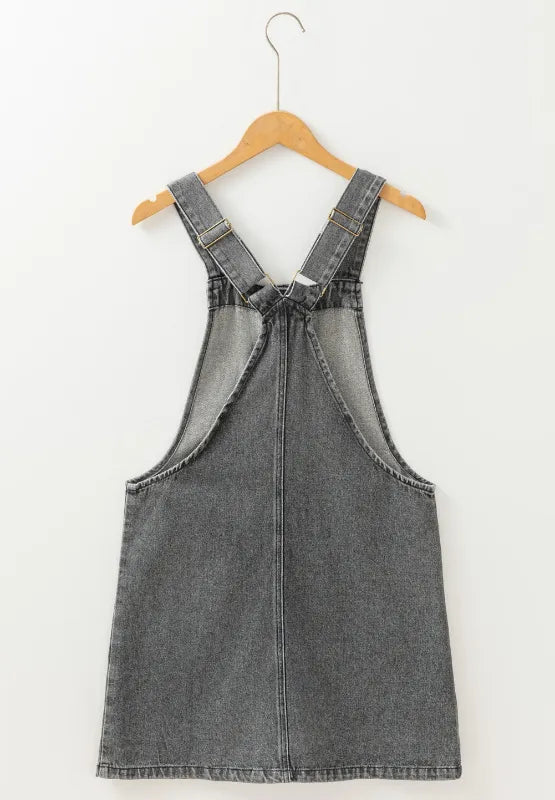 Wide Strap Button Down Denim Overall Dress hanging on a wooden hanger against a white background.