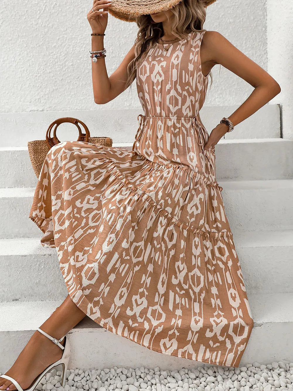 Perfee Frill Cutout Printed Round Neck Sleeveless Dress worn by a woman sitting on steps, showcasing its elegant design.