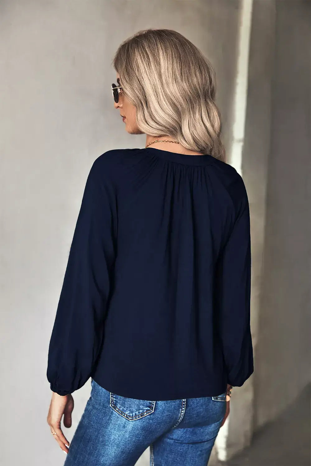 Back view of a woman wearing a navy tie neck long sleeve blouse with long sleeves and relaxed fit.
