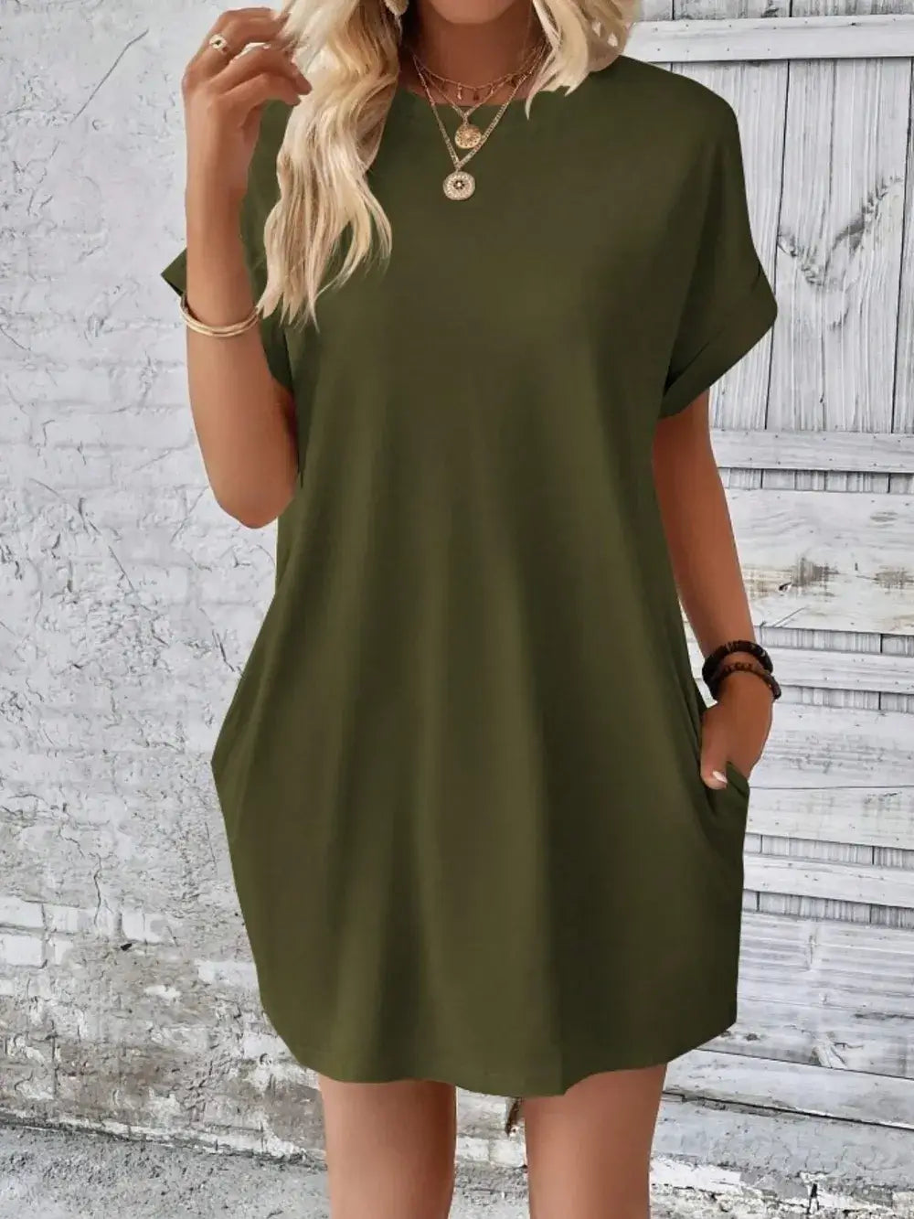Olive green pocketed round neck short sleeve dress displayed against a rustic background.