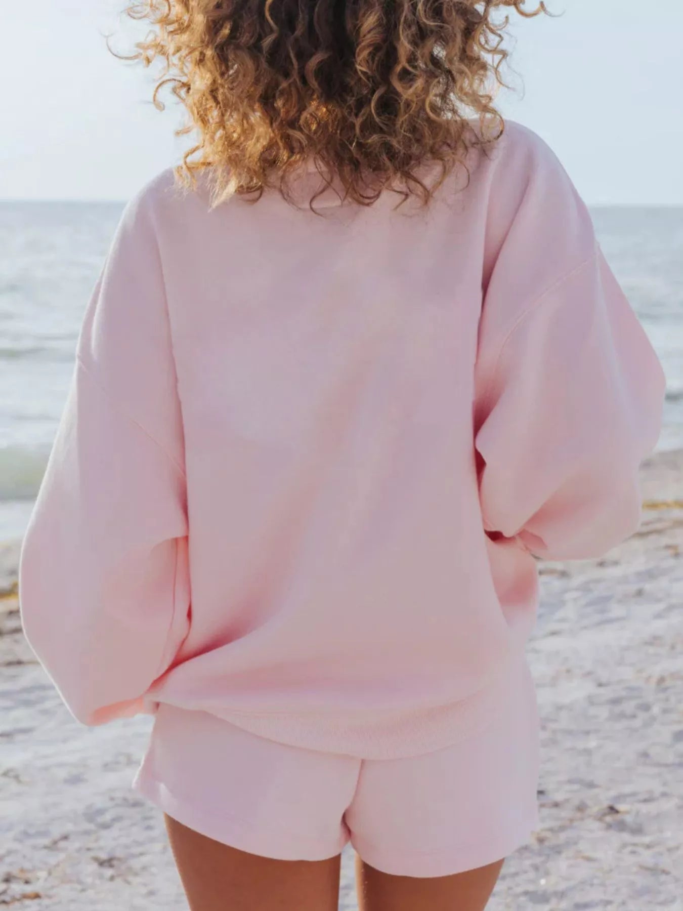 Relaxed Fit Round Neck Sweatshirt and Shorts Set in soft pink, worn by a woman outdoors by the beach.