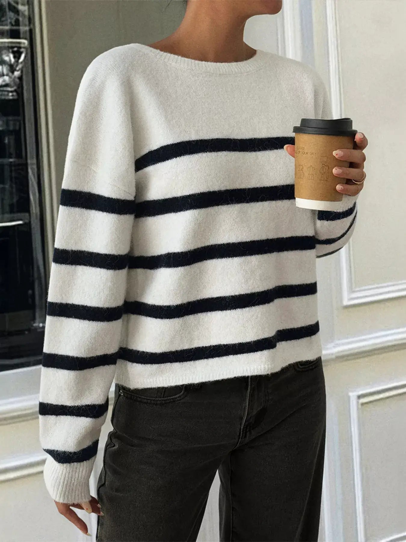 Striped round neck long sleeve knit top worn with black jeans, holding a coffee cup, showcasing a casual chic look.