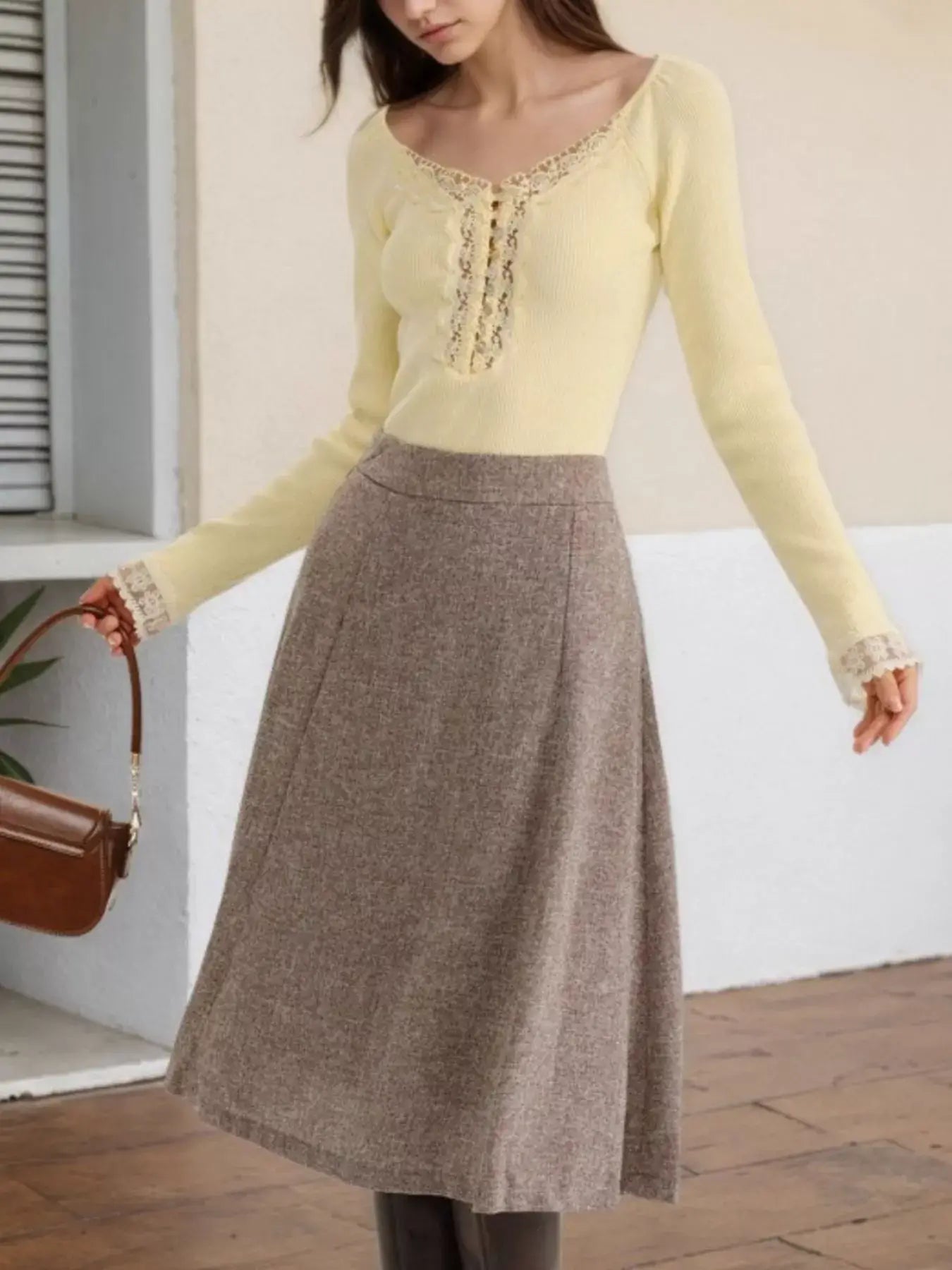 Woman wearing a yellow lace trim long sleeve top with a brown skirt in a stylish outfit.