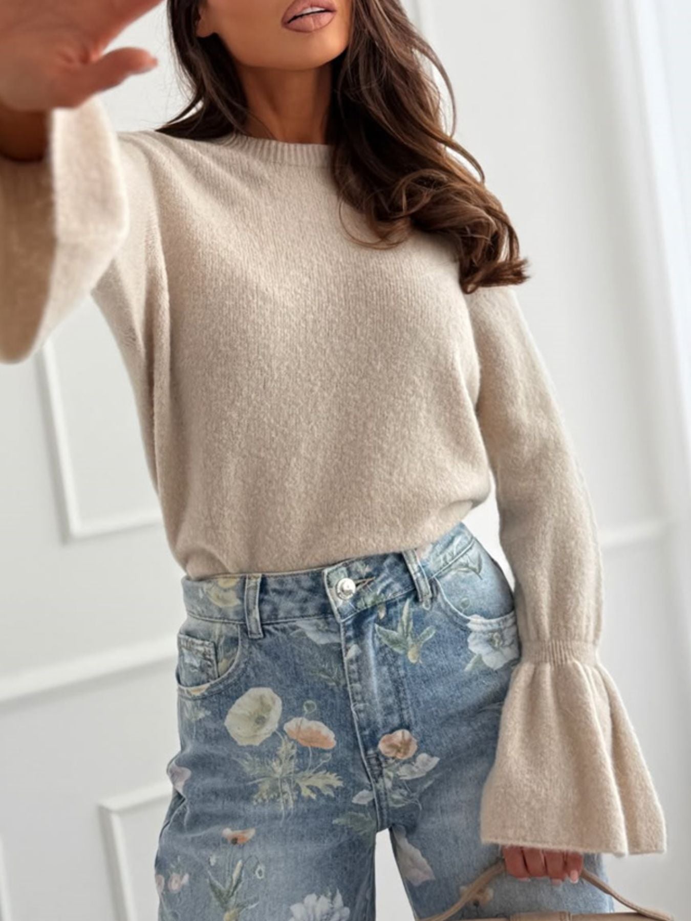 A model showcasing a Round Neck Flounce Sleeve Sweater, an elegant women's ribbed knit item, paired with stylish floral jeans.
