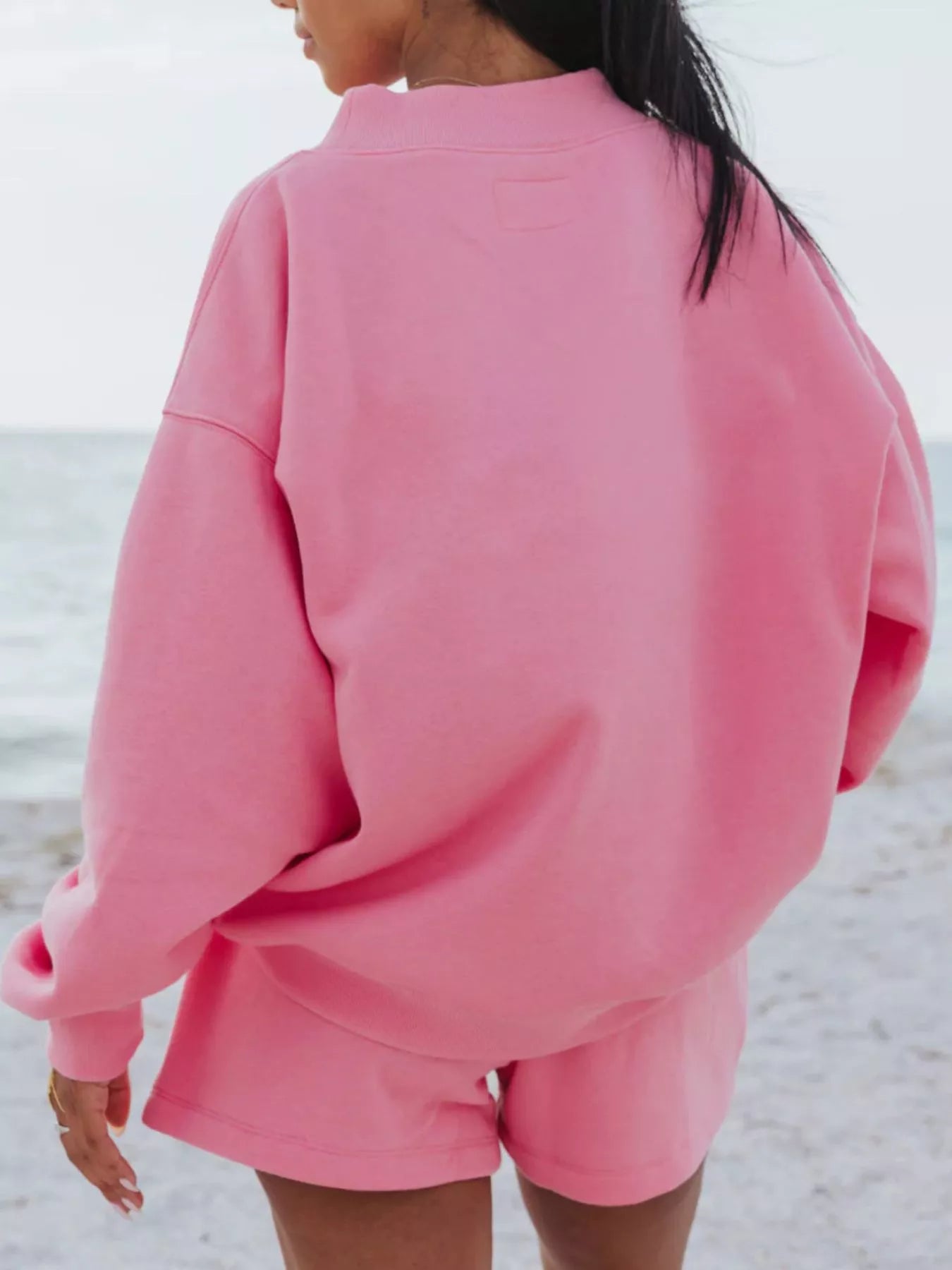 Model wearing a Relaxed Fit Round Neck Sweatshirt and Shorts Set in pink at the beach, showcasing casual style.