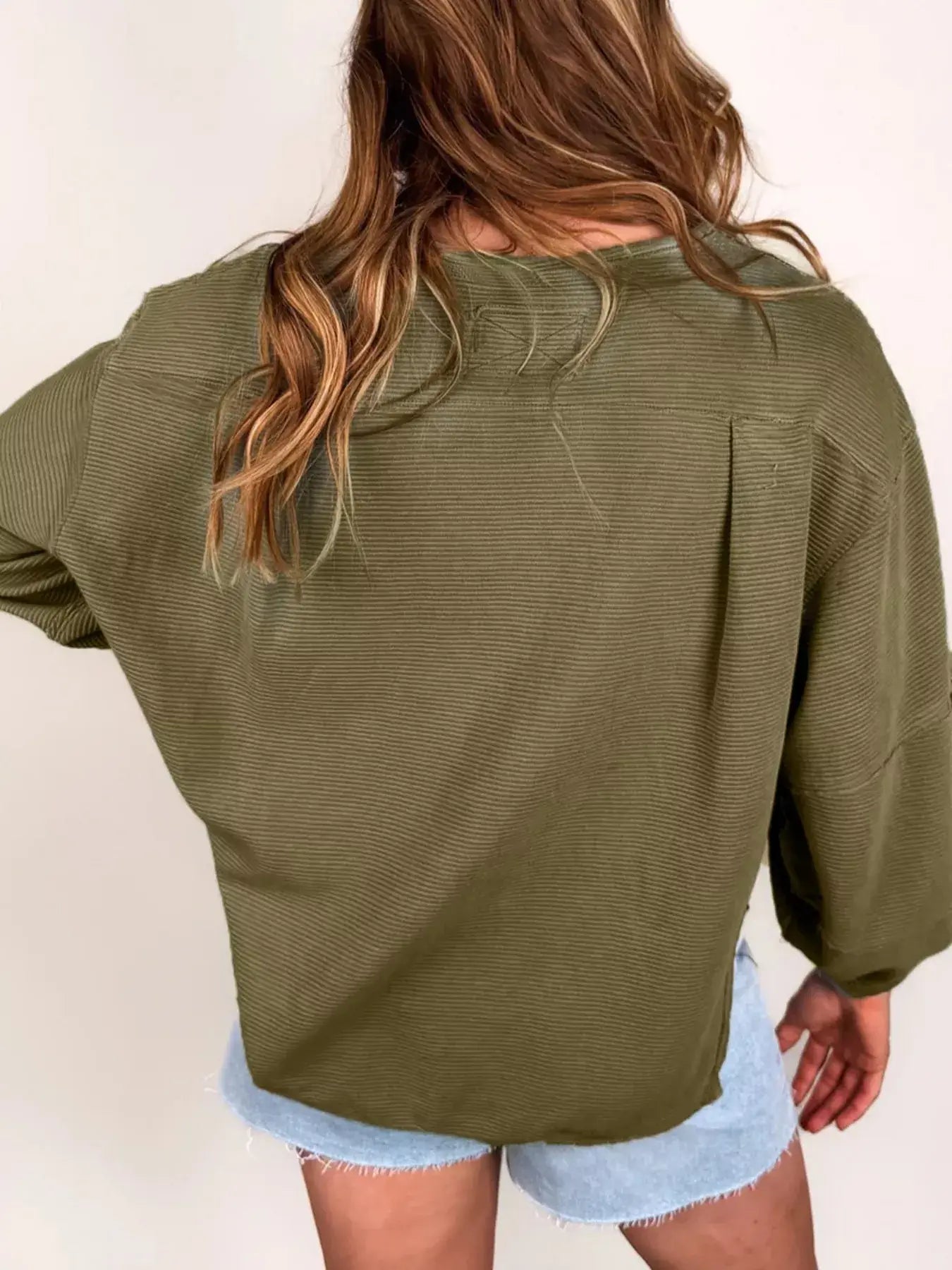 Back view of a woman wearing a Ribbed Knit Oversized Sweatshirt in olive green, styled with denim shorts.