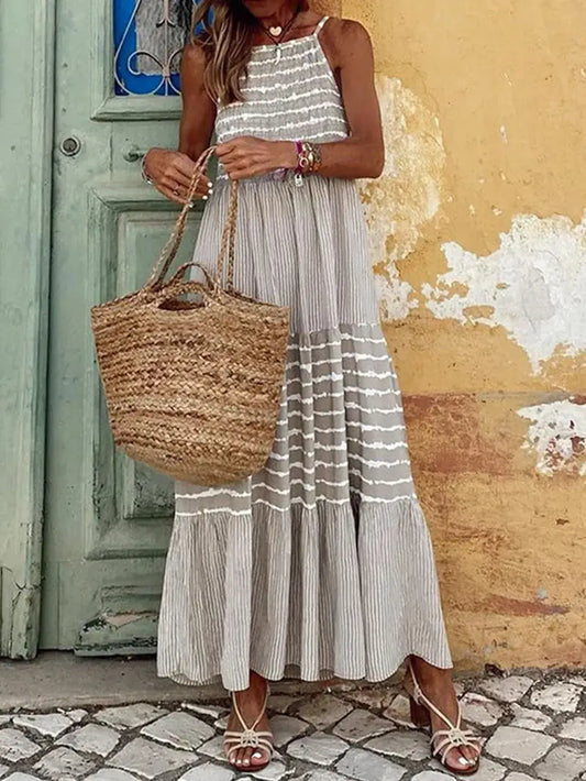 Woman in a Tiered Striped Sleeveless Cami Dress holding a straw bag, set against a vibrant wall, ideal for summer style.
