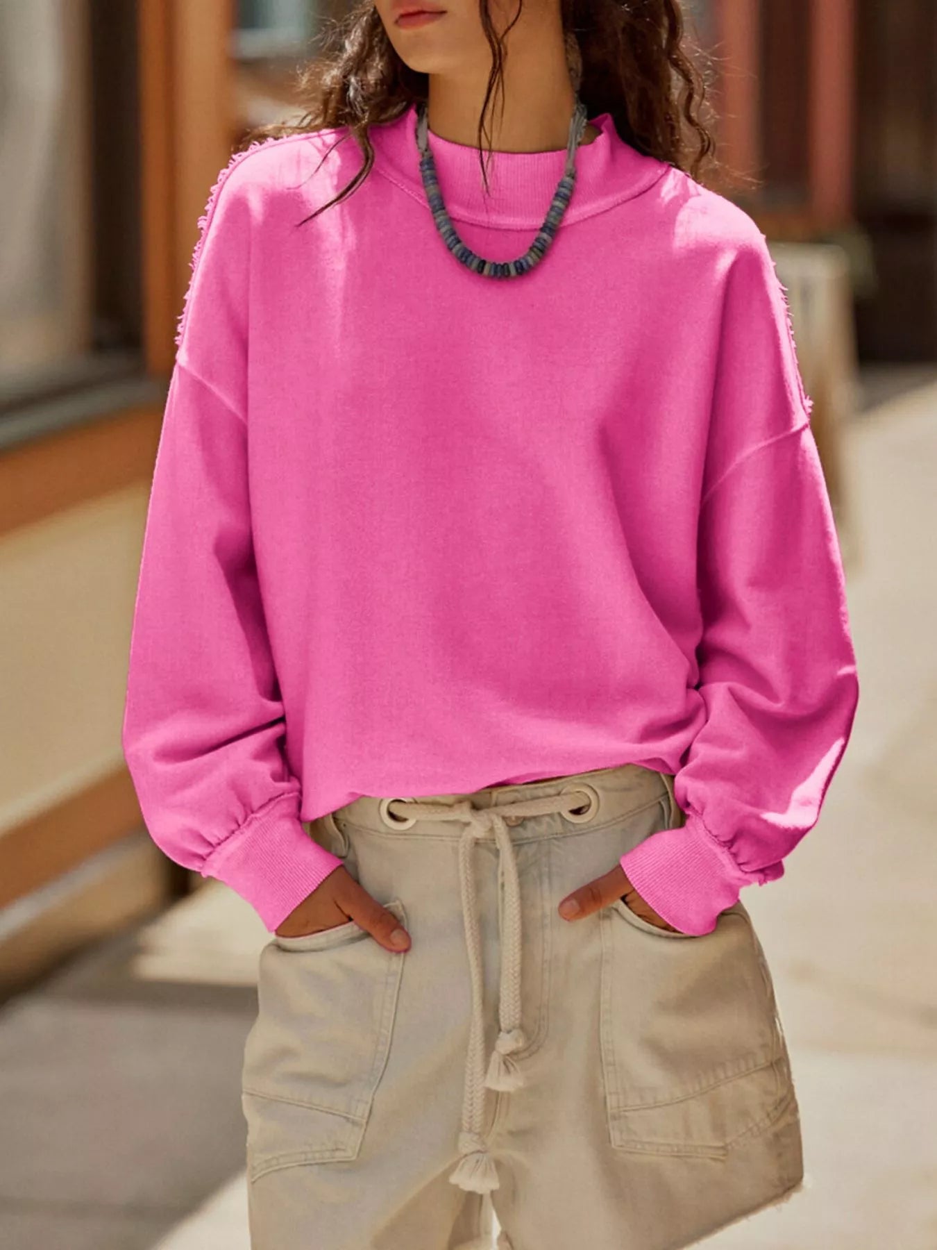 Exposed Seam Dropped Shoulder Sweatshirt in vibrant pink worn casually with shorts and a necklace.