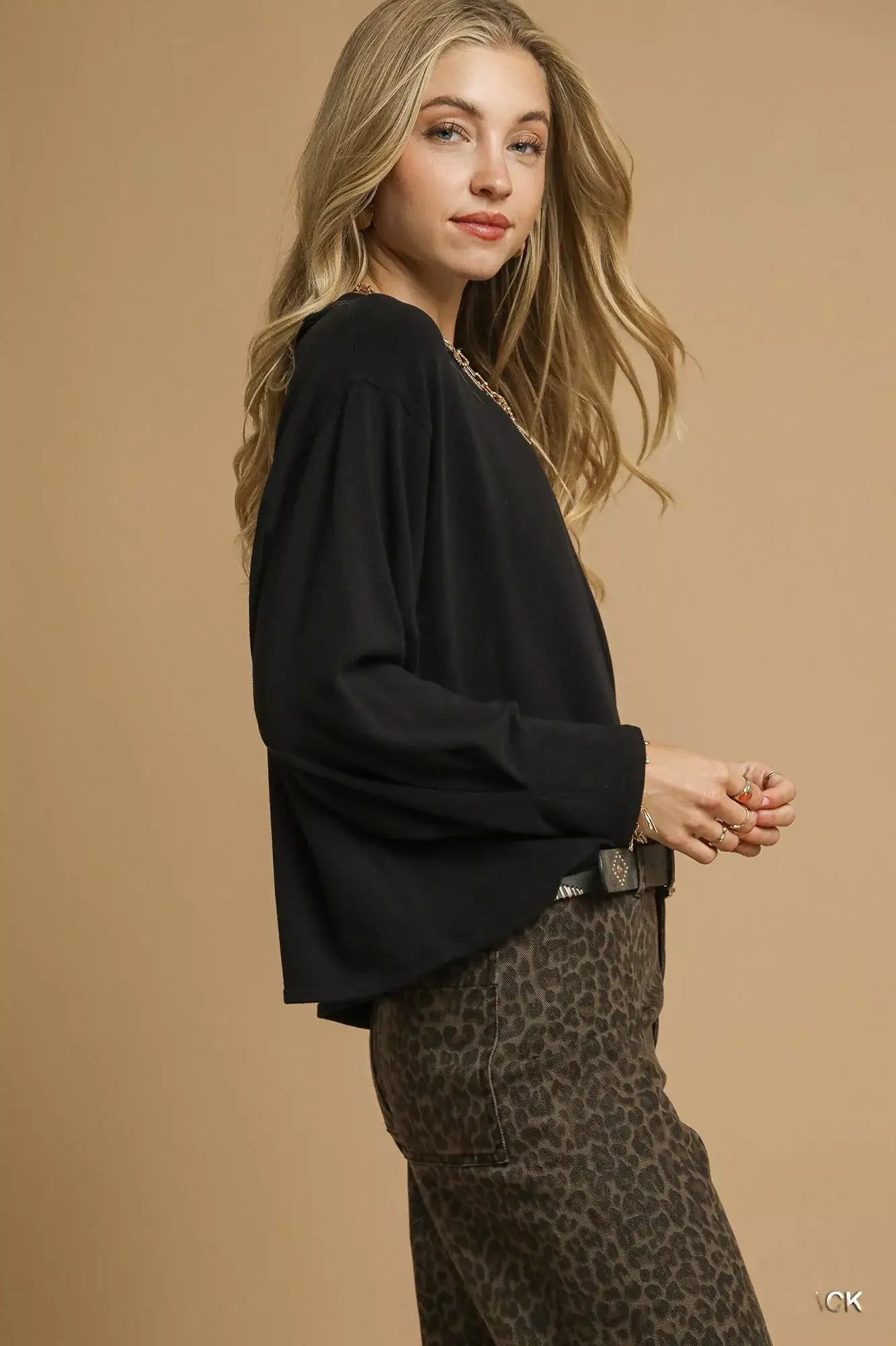 Model wearing a black oversized crewneck top paired with leopard print pants against a beige background.