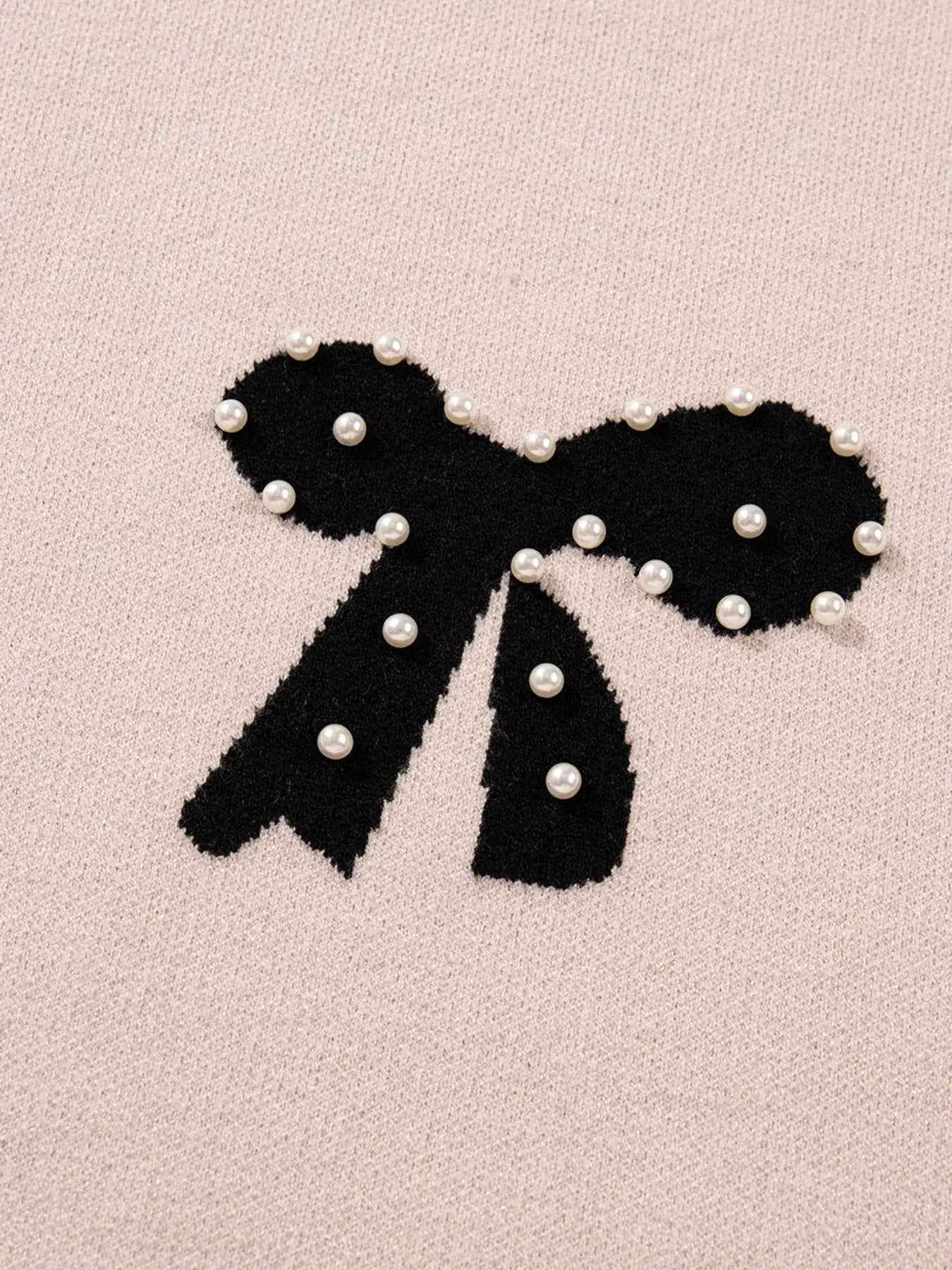 Close-up of the pearl embellished bow pattern loose sweater showcasing a delicate bow design with pearl accents.