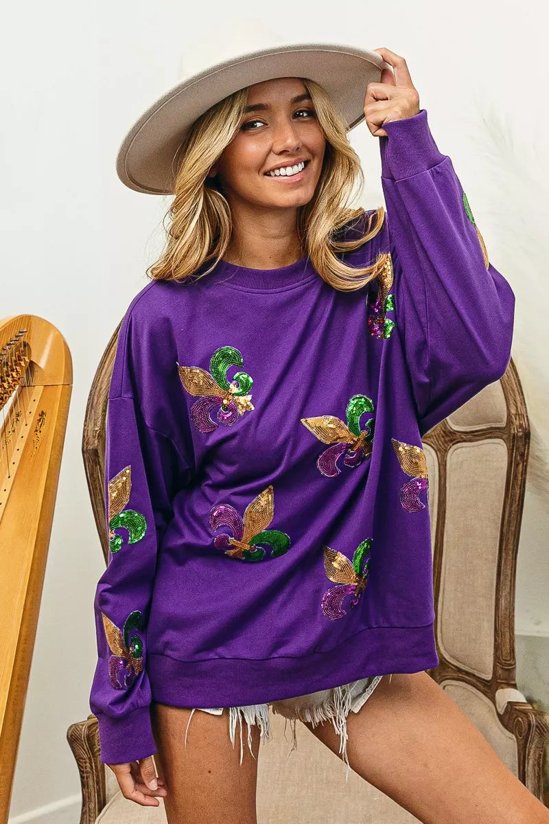 BiBi Fleur De Lis Sequin Patches Mardi Gras Sweatshirt in purple with sequins, shown on a smiling model.