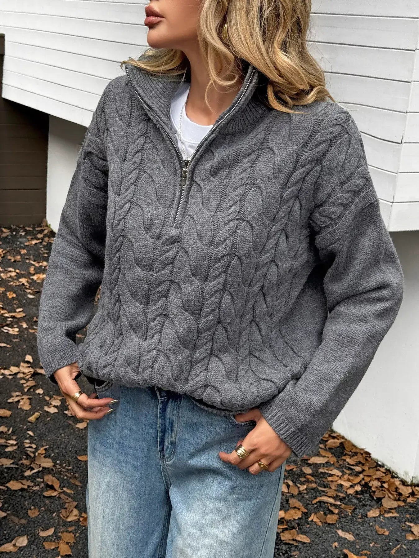 Woman wearing a zip collar cable-knit sweater in gray, showcasing a stylish zip-up design and cable-knit texture.