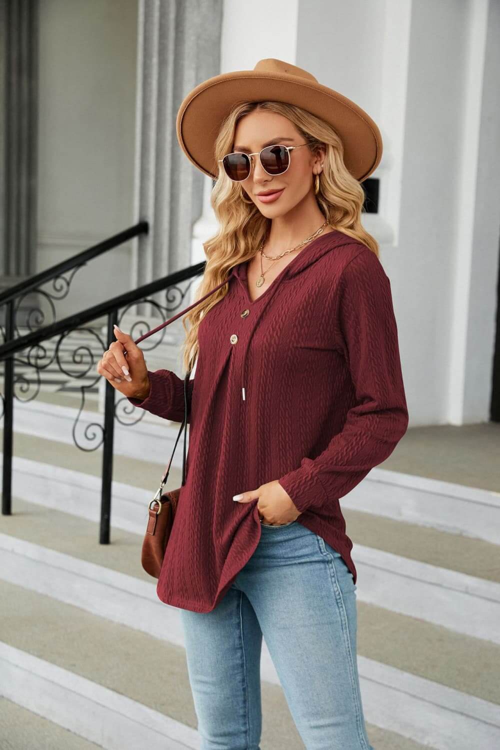 Model wearing Long Sleeve Hooded Blouse in burgundy, styled with denim jeans and a hat.