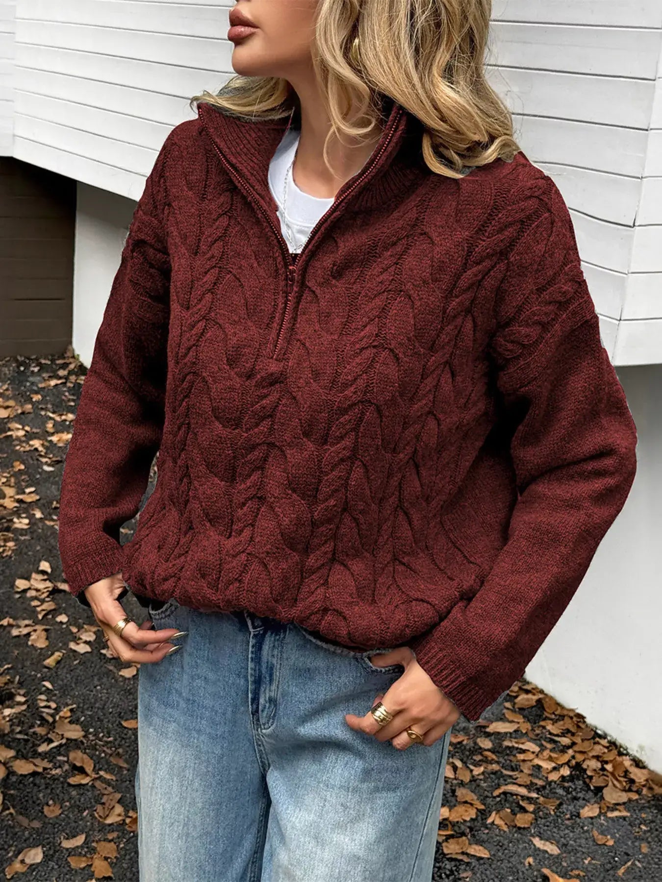 Woman wearing a zip collar cable-knit sweater in burgundy with a relaxed fit, enjoying fall outdoors.