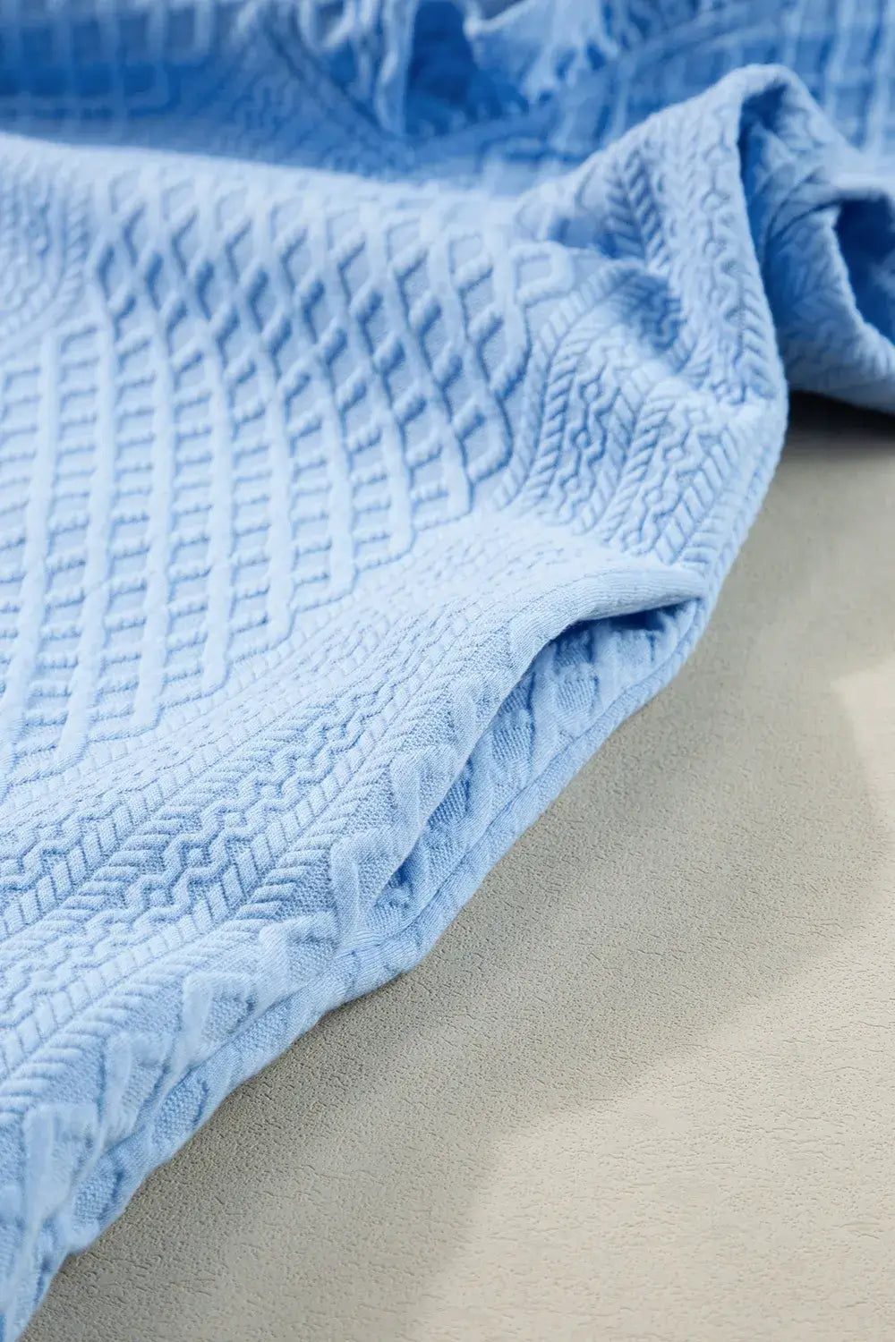 Close-up of light blue textured fabric showcasing a quilted pattern, ideal for stylish garment design.