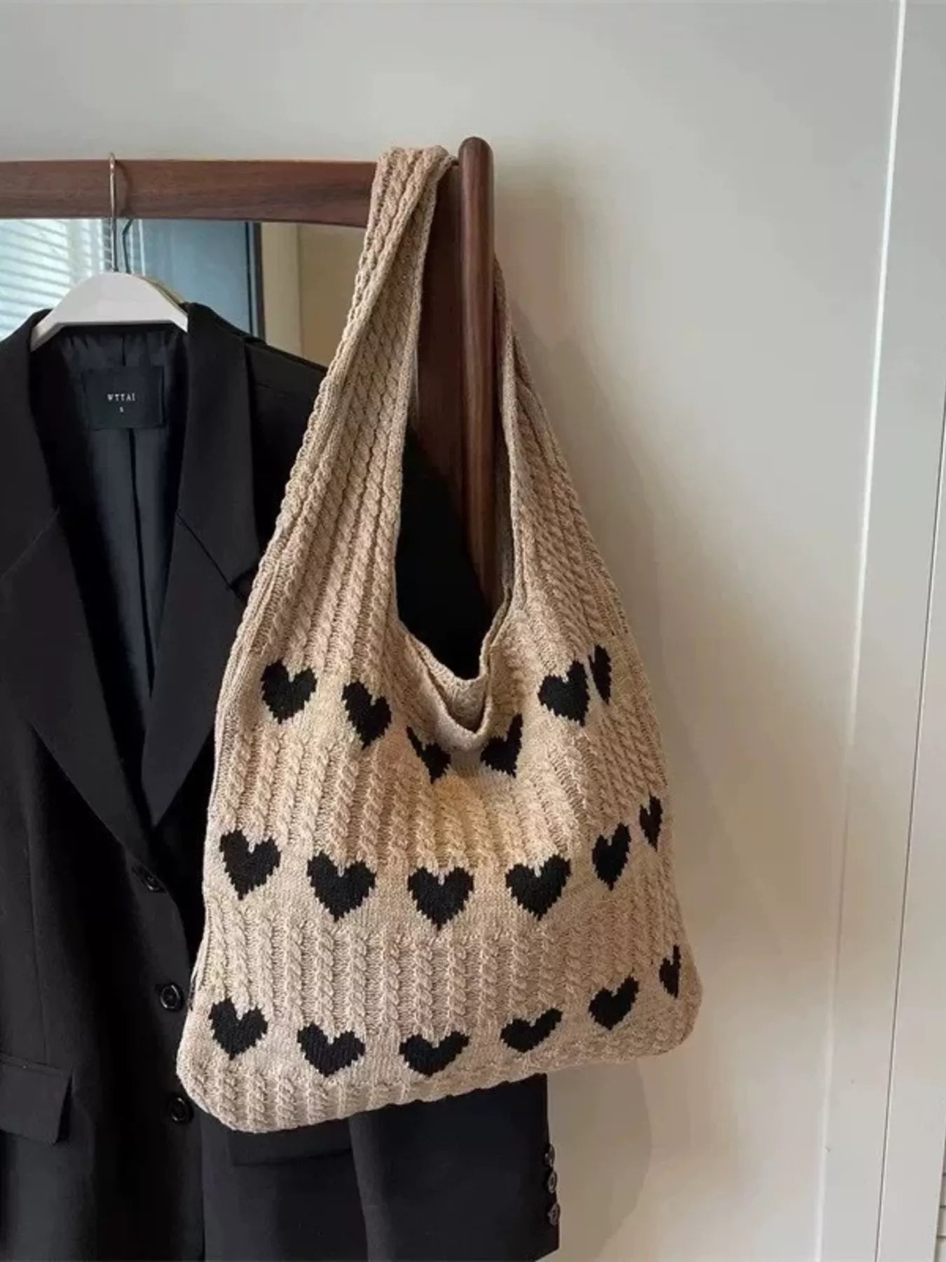 Heart Pattern Knitted Handbag hanging on a wooden hanger against a black jacket.