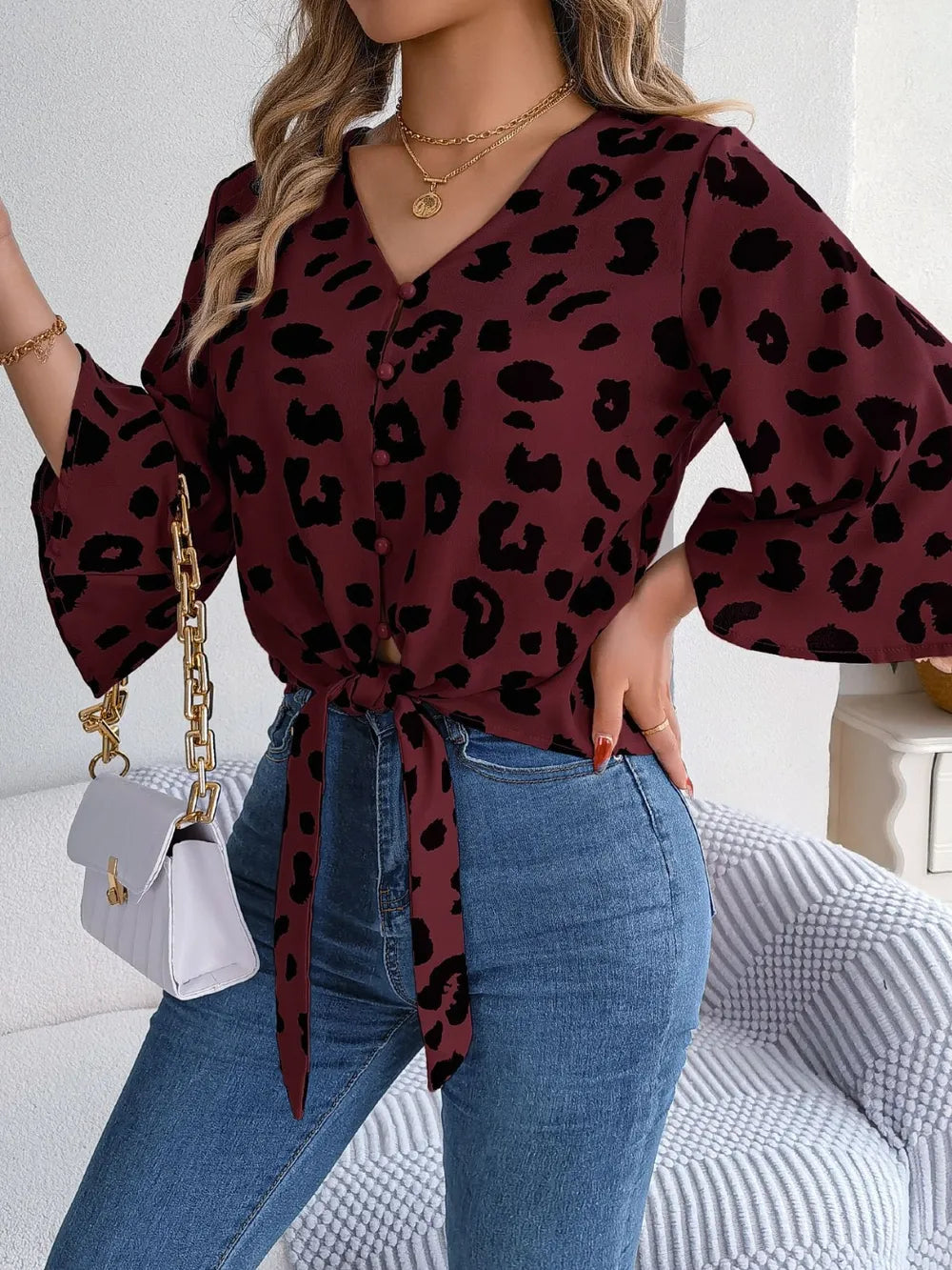 Tied Button Up Leopard V-Neck Blouse styled with denim and a white handbag, showcasing its buttoned and tied features.