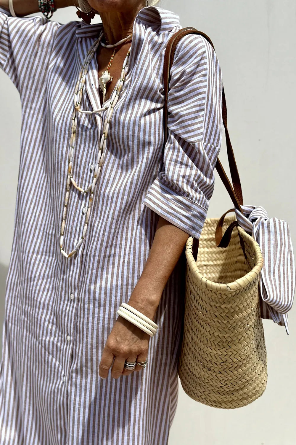 Woman wearing a Tied Button Up Three-Quarter Sleeve Dress with striped pattern and a woven bag.