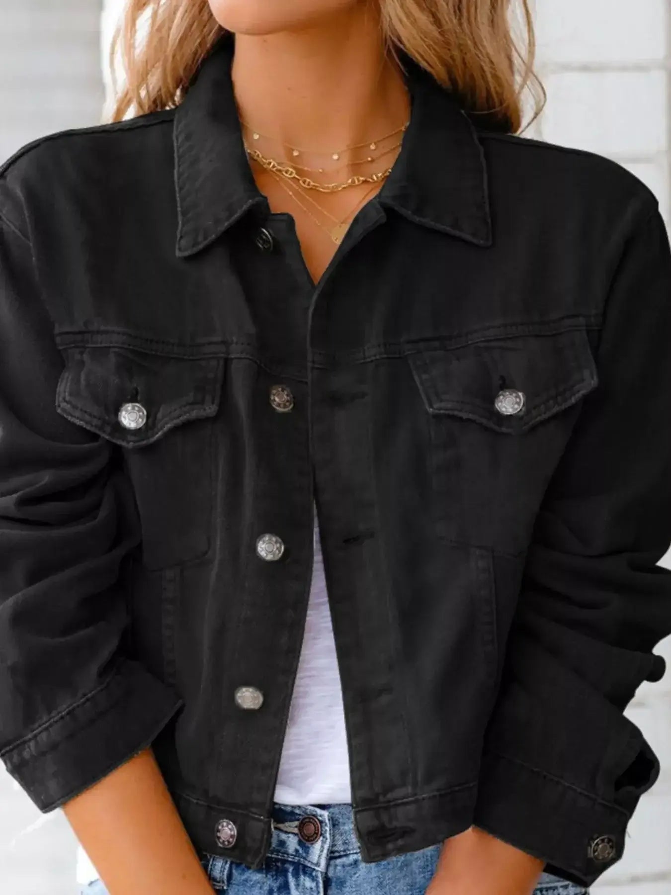 Woman wearing a button-up long sleeve black denim jacket with a classic cut and front pockets.