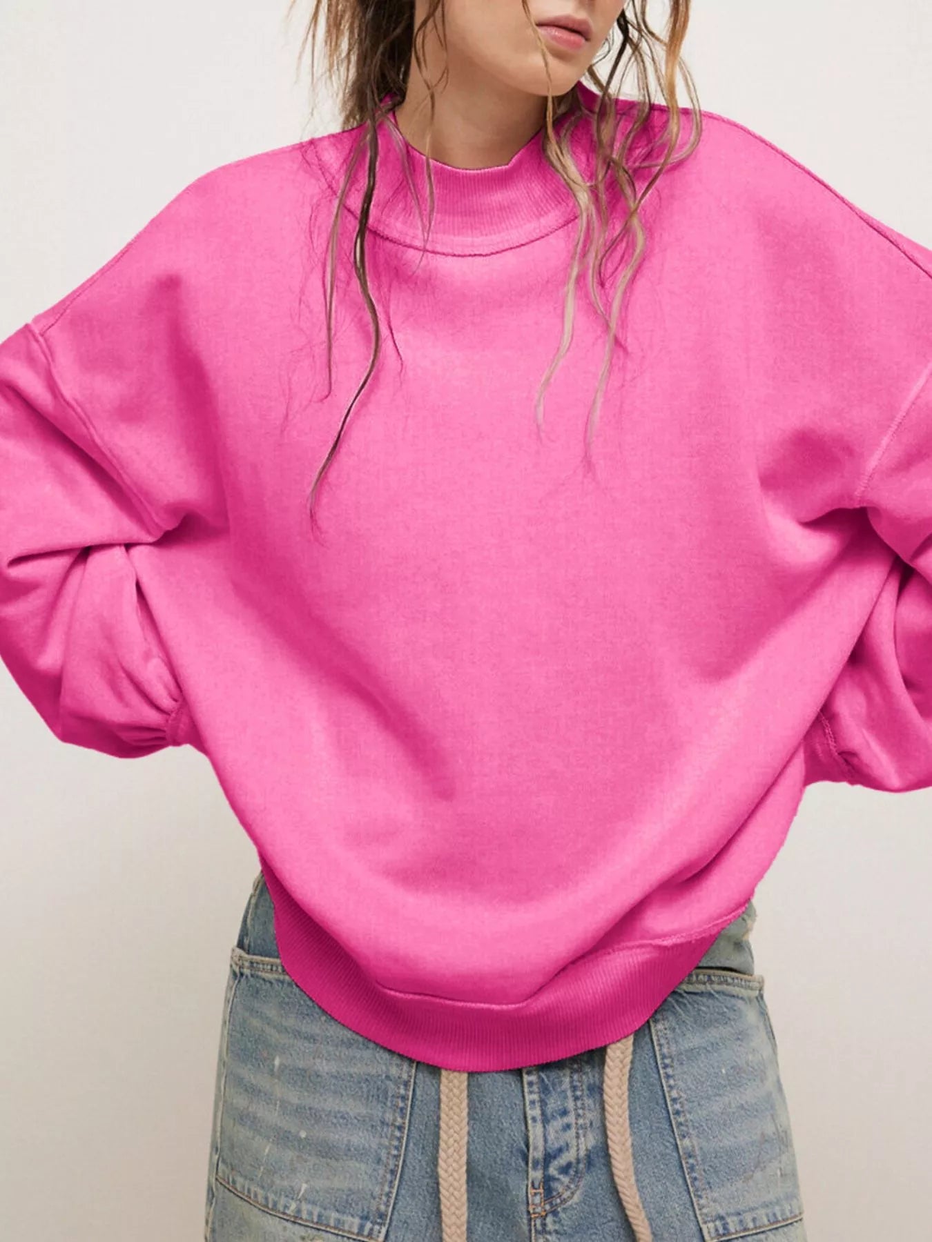 Exposed Seam Dropped Shoulder Sweatshirt in vibrant pink worn by a woman with wavy hair, showcasing a casual look.