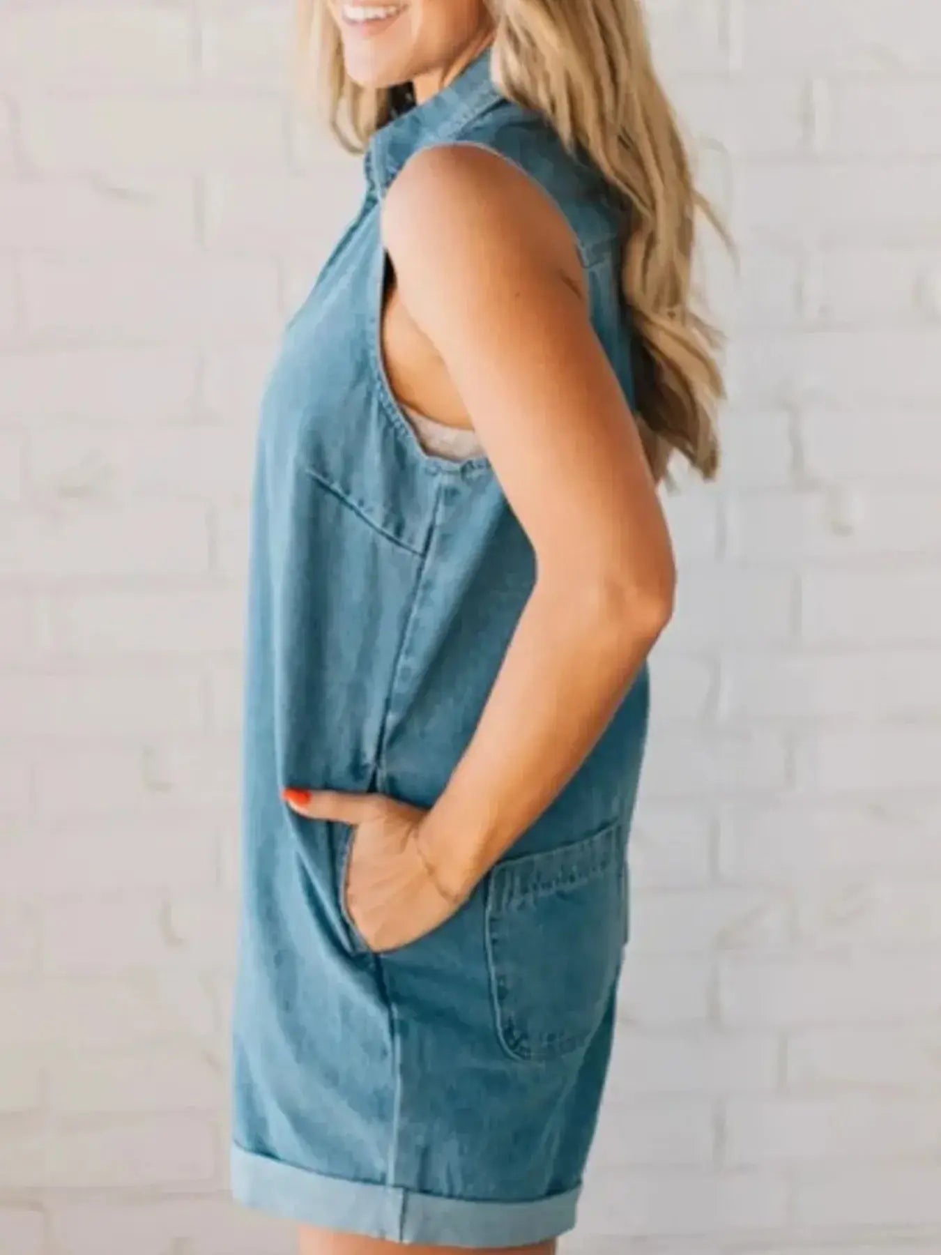 Side view of a woman wearing a sleeveless zip front denim romper with pockets, styled for casual summer wear.