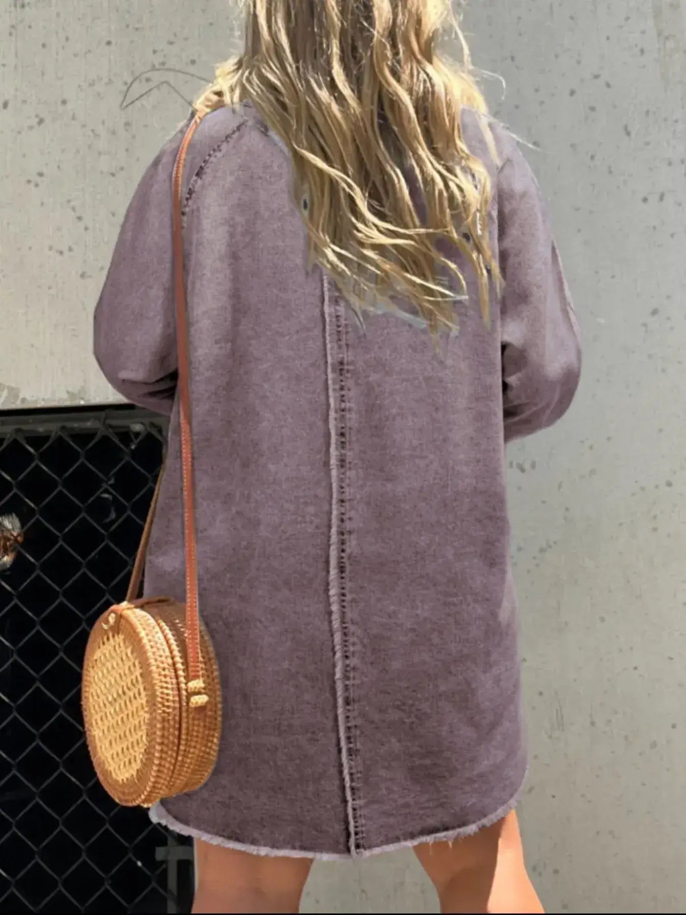 Back view of a model in a relaxed purple denim shirt dress with a woven crossbody bag.