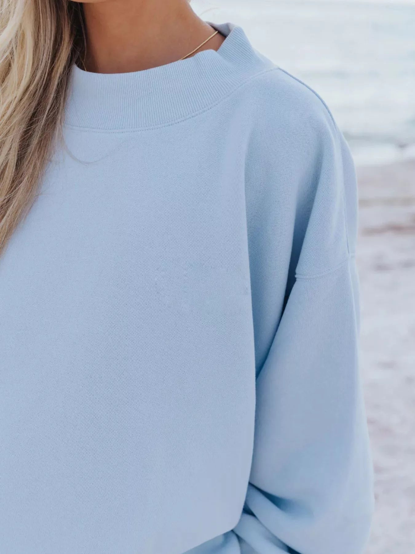 Relaxed Fit Round Neck Sweatshirt and Shorts Set showcasing light blue sweatshirt detail against a beach backdrop.