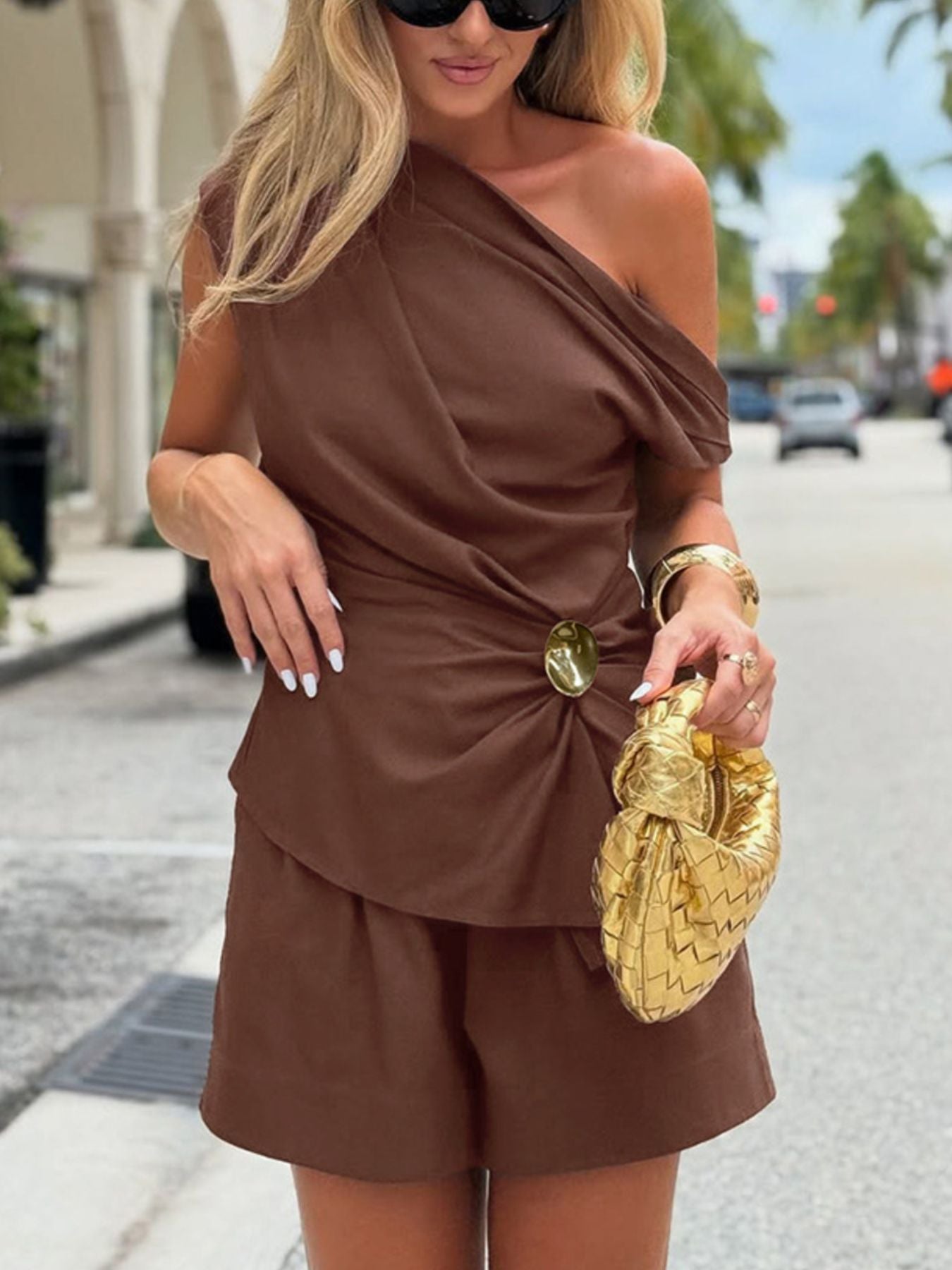 One Shoulder Top and Shorts Set in brown featuring an asymmetrical design, ruched detailing, and a stylish golden bag.