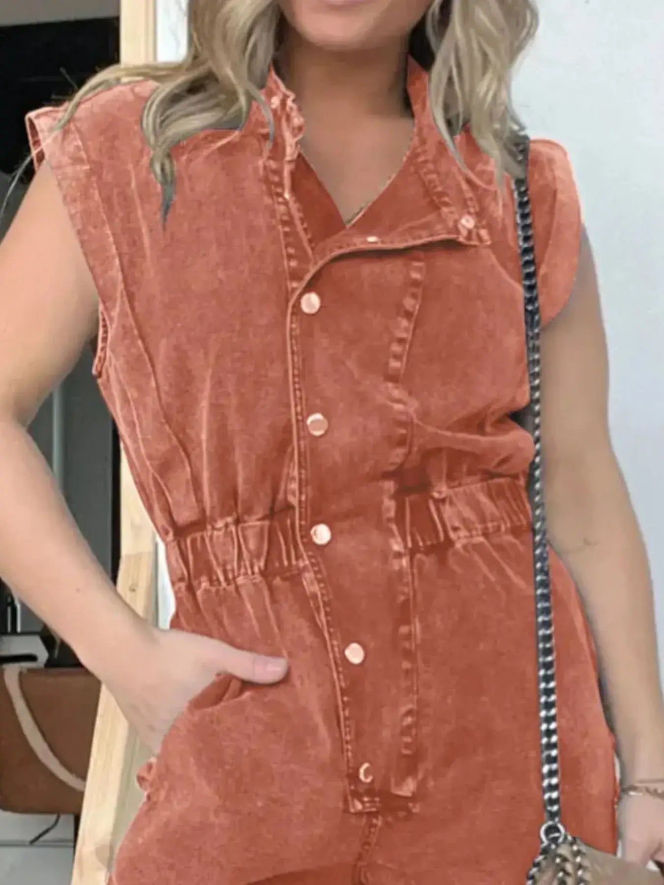 Model wearing a plus size button front cap sleeve denim jumpsuit in rust color with a belted waist and practical pockets.