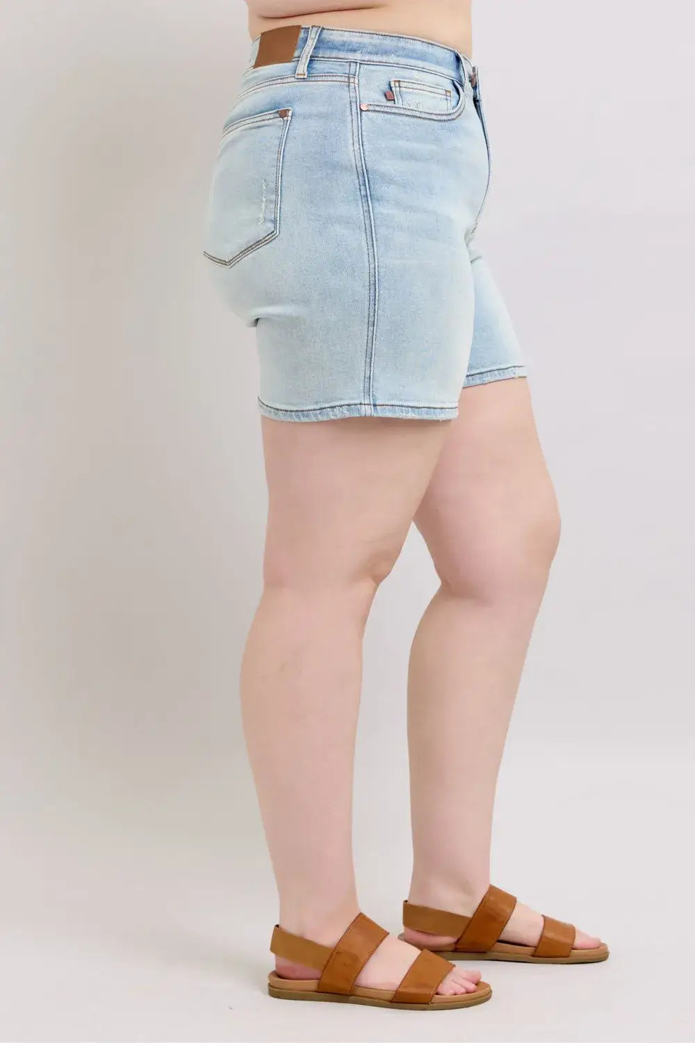 Side view of women’s plus size Judy Blue denim shorts with pockets and a 2-button closure, styled with sandals.