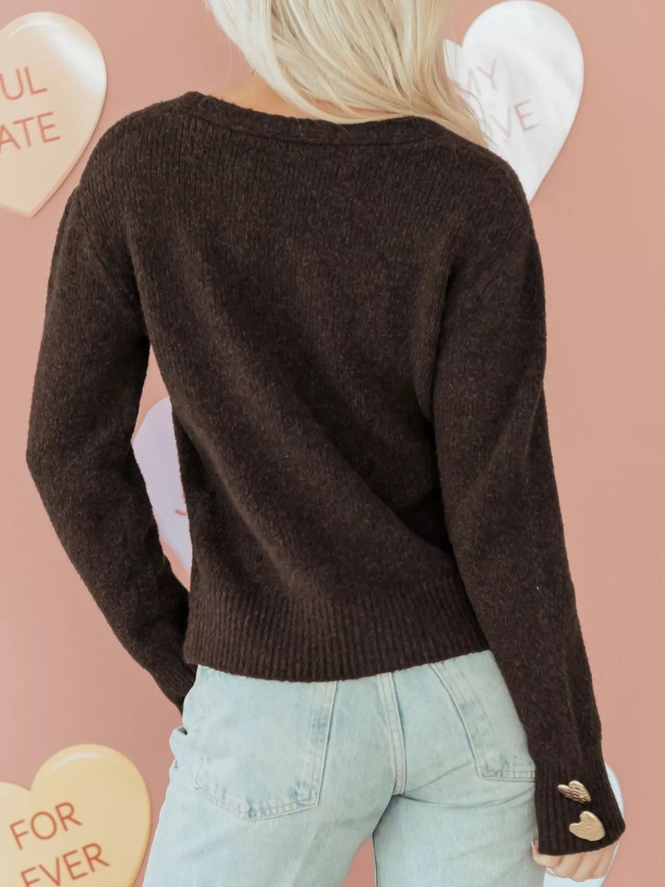 Heart Metal Button V Neck Cardigan Sweater back view on a woman with light hair against a pastel background.