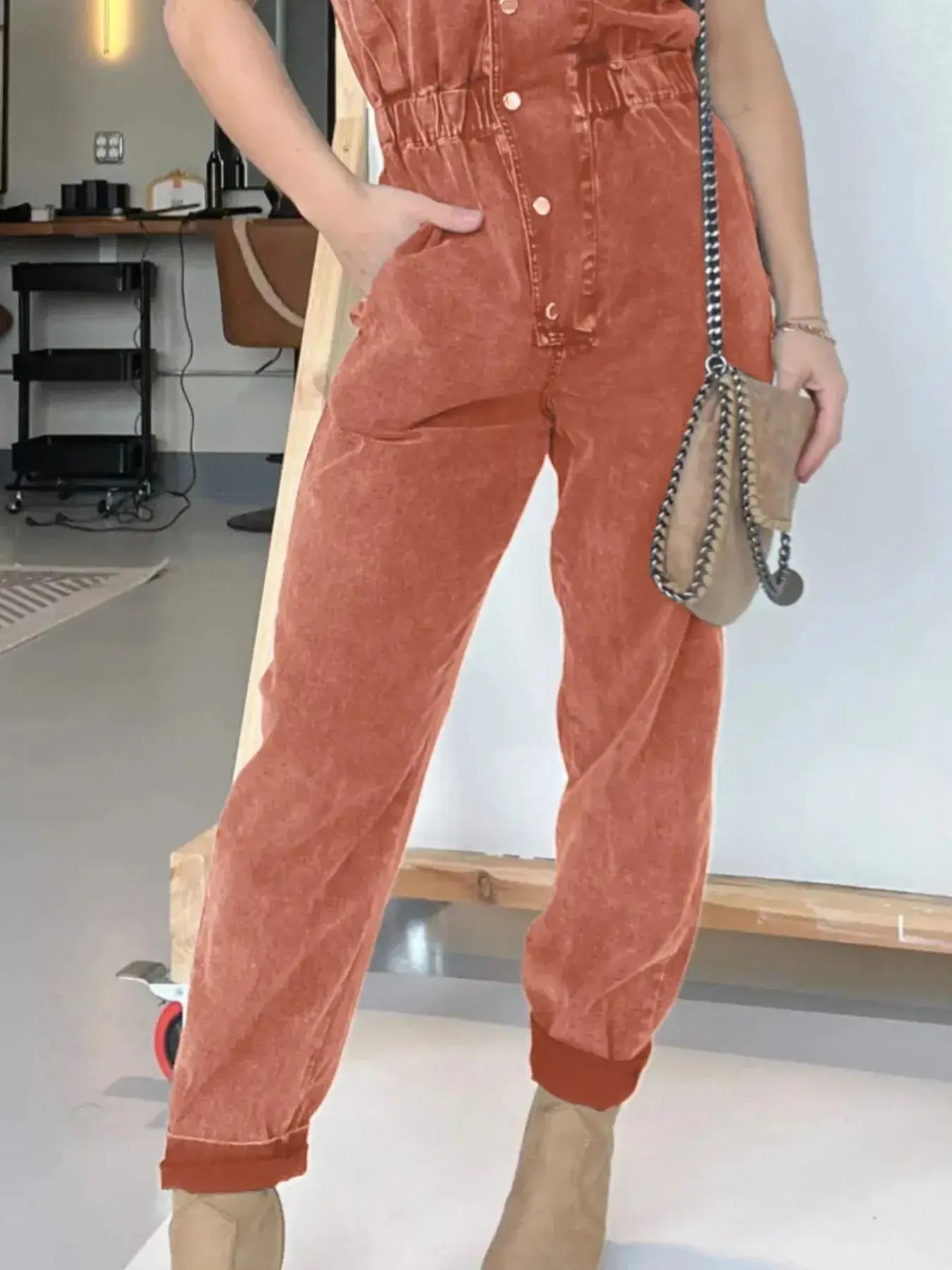 Model wearing a stylish rust-colored button front denim jumpsuit with pockets and a belted waist.