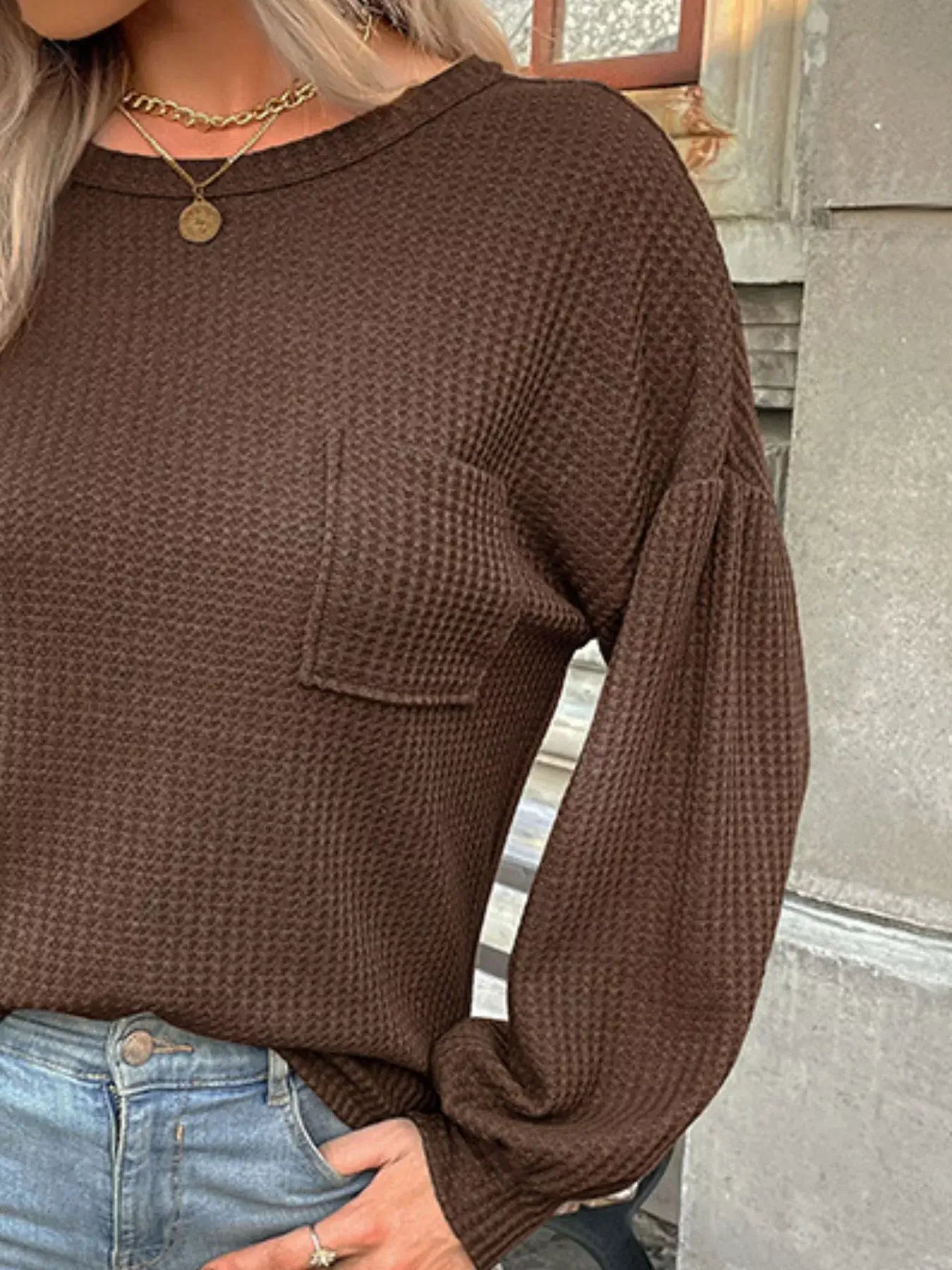 Waffle knit brown round neck top with long sleeves and pocket, styled with jeans for a cozy look.