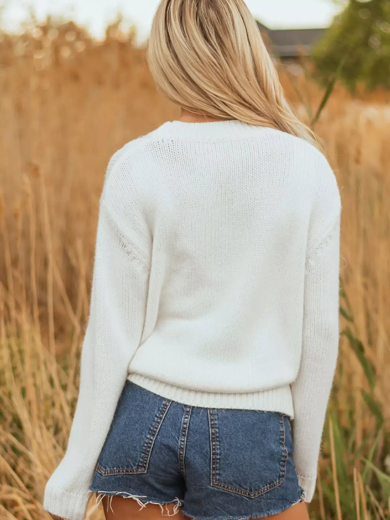 Back view of the embroidered bow boots graphic drop shoulder sweater paired with denim shorts in a natural setting.