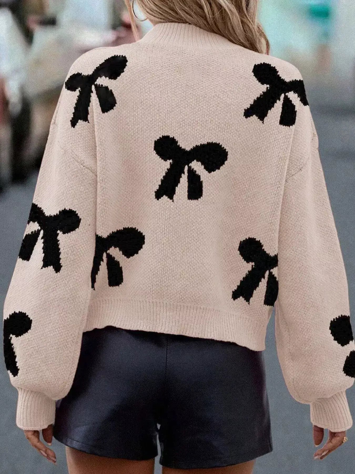 Pearl embellished bow pattern loose sweater in a cozy knit with black bows on a pink background, perfect for stylish layering.