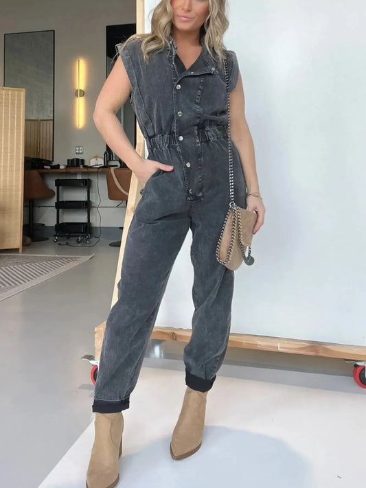 Model wearing a plus size button front cap sleeve denim jumpsuit, styled with a handbag and ankle boots.