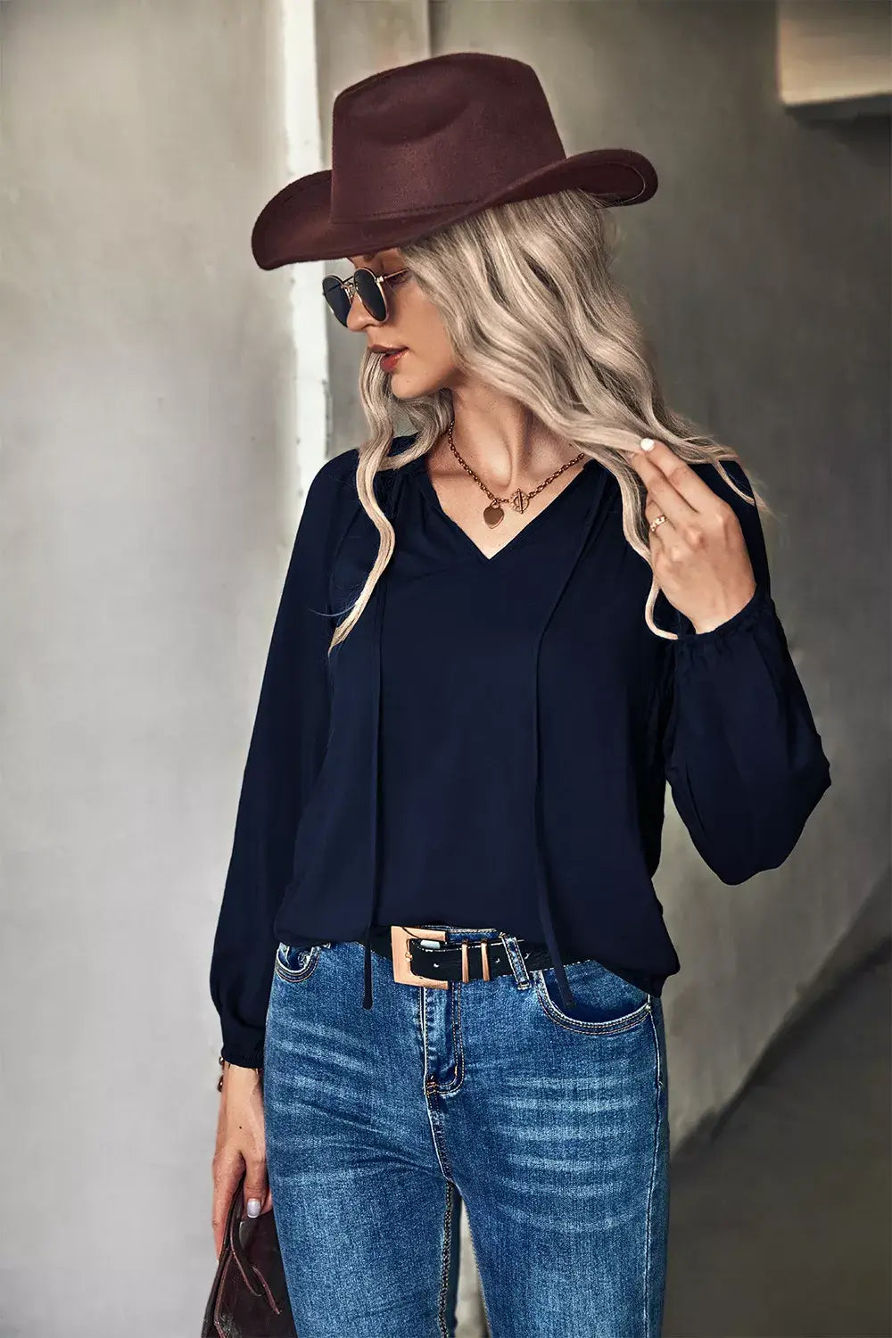 Woman wearing a tie neck long sleeve blouse with jeans and a hat, showcasing elegant office wear style.